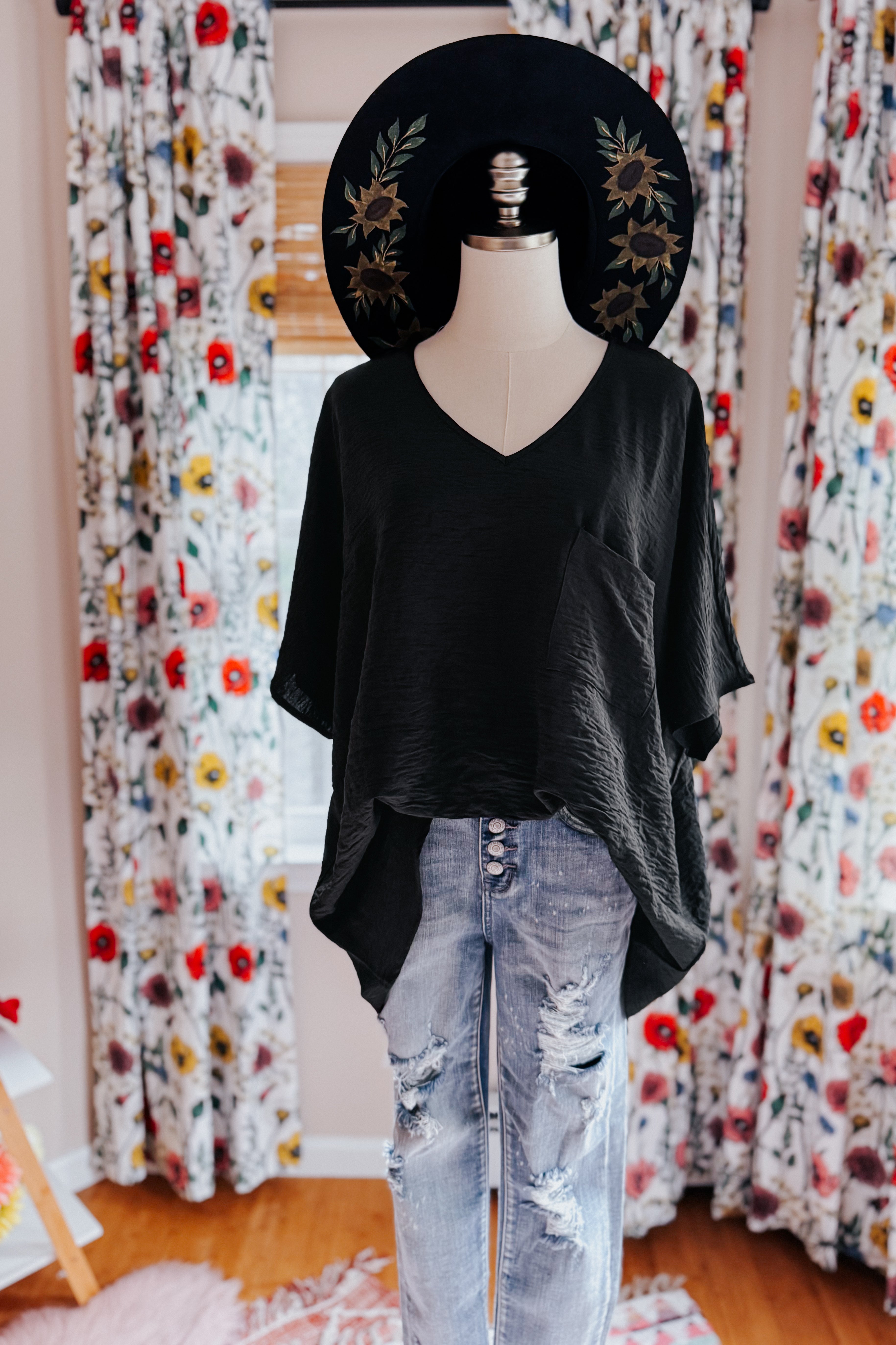 Mannequin dressed in loose black V-neck top with short sleeves paired with distressed blue jeans indoors