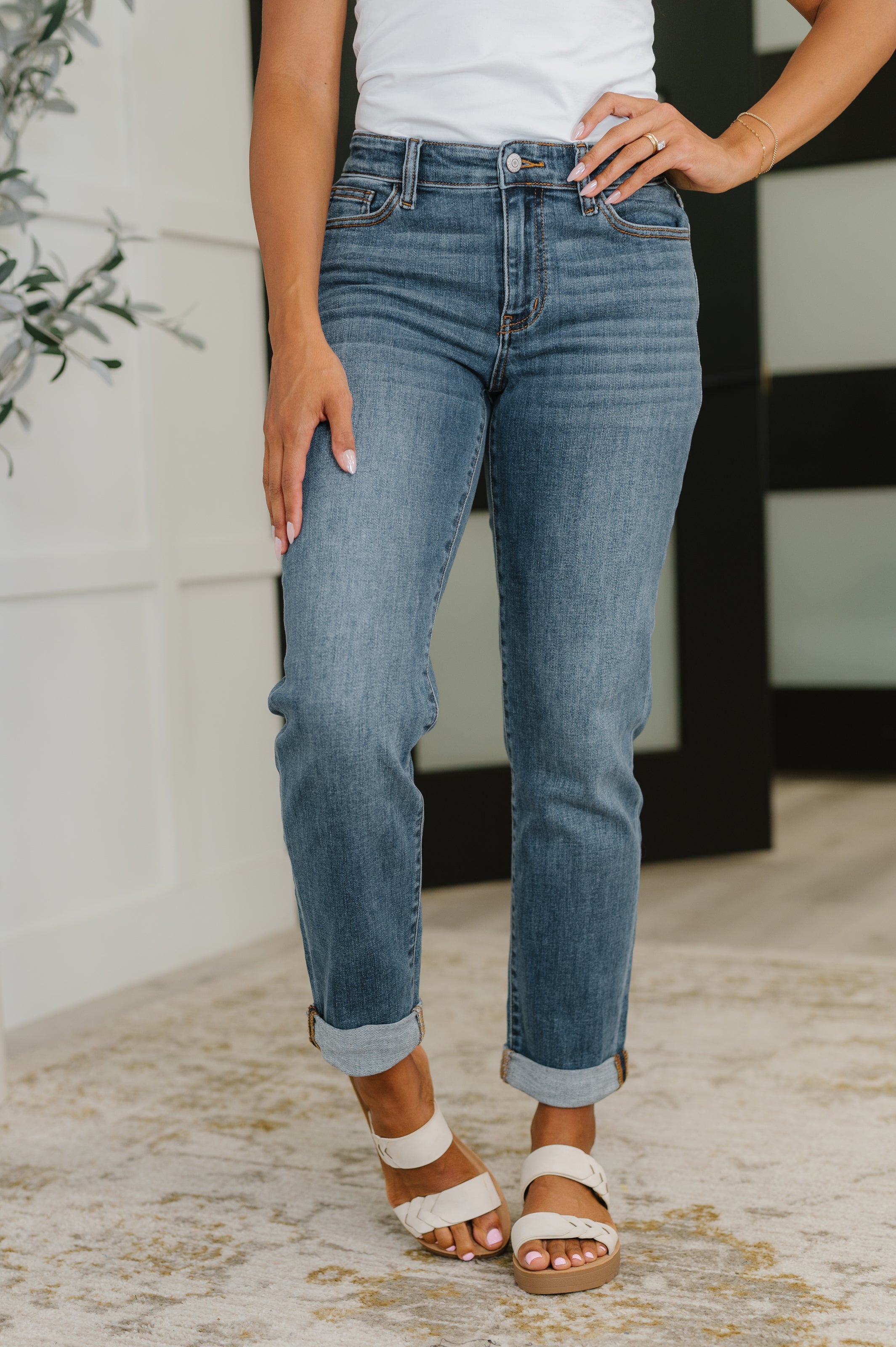 Woman wearing blue mid rise boyfriend jeans with rolled cuffs and white sandals indoors