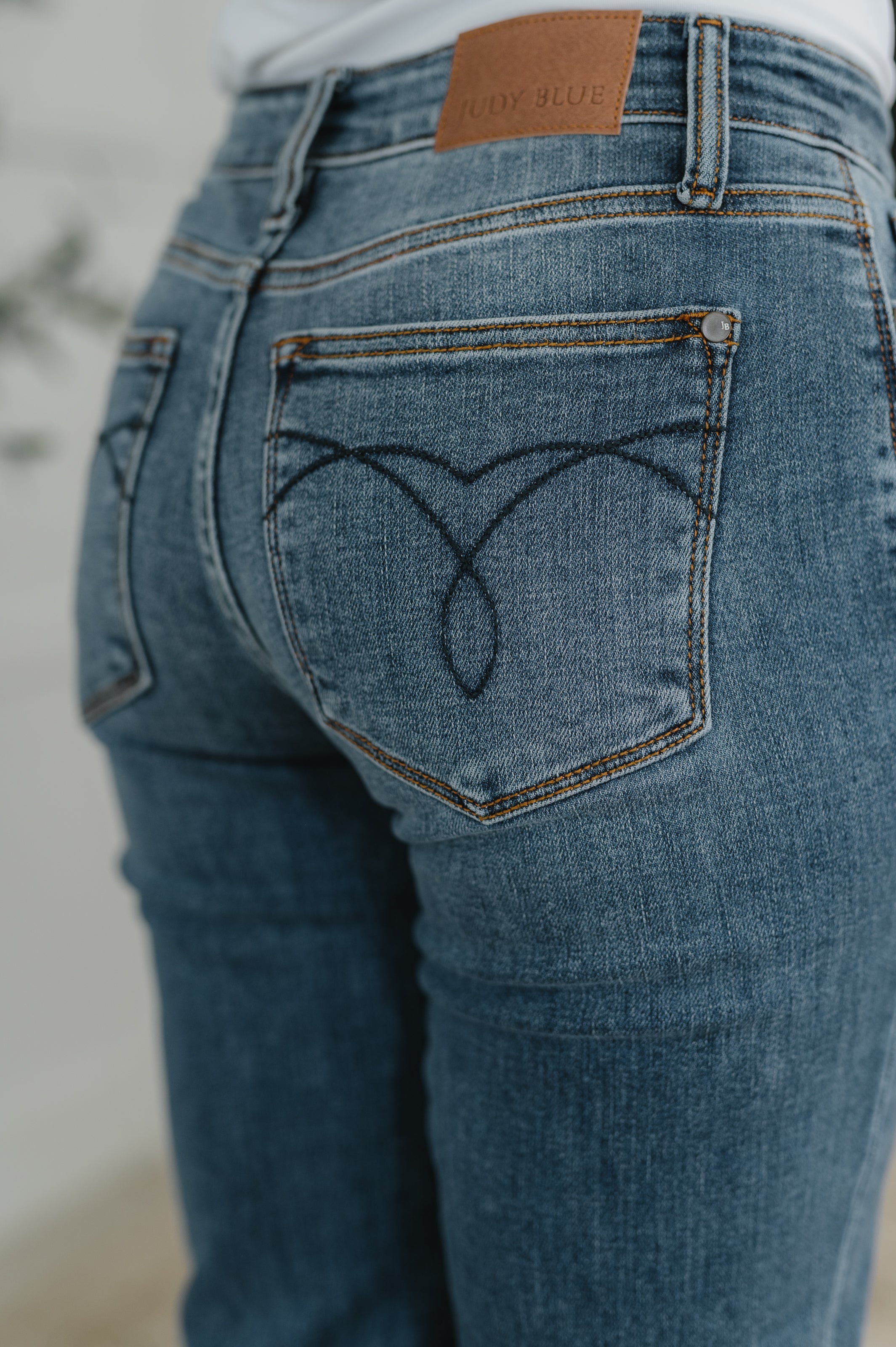 Close view of blue jeans with a back pocket featuring decorative curved stitching and a zippered top seam