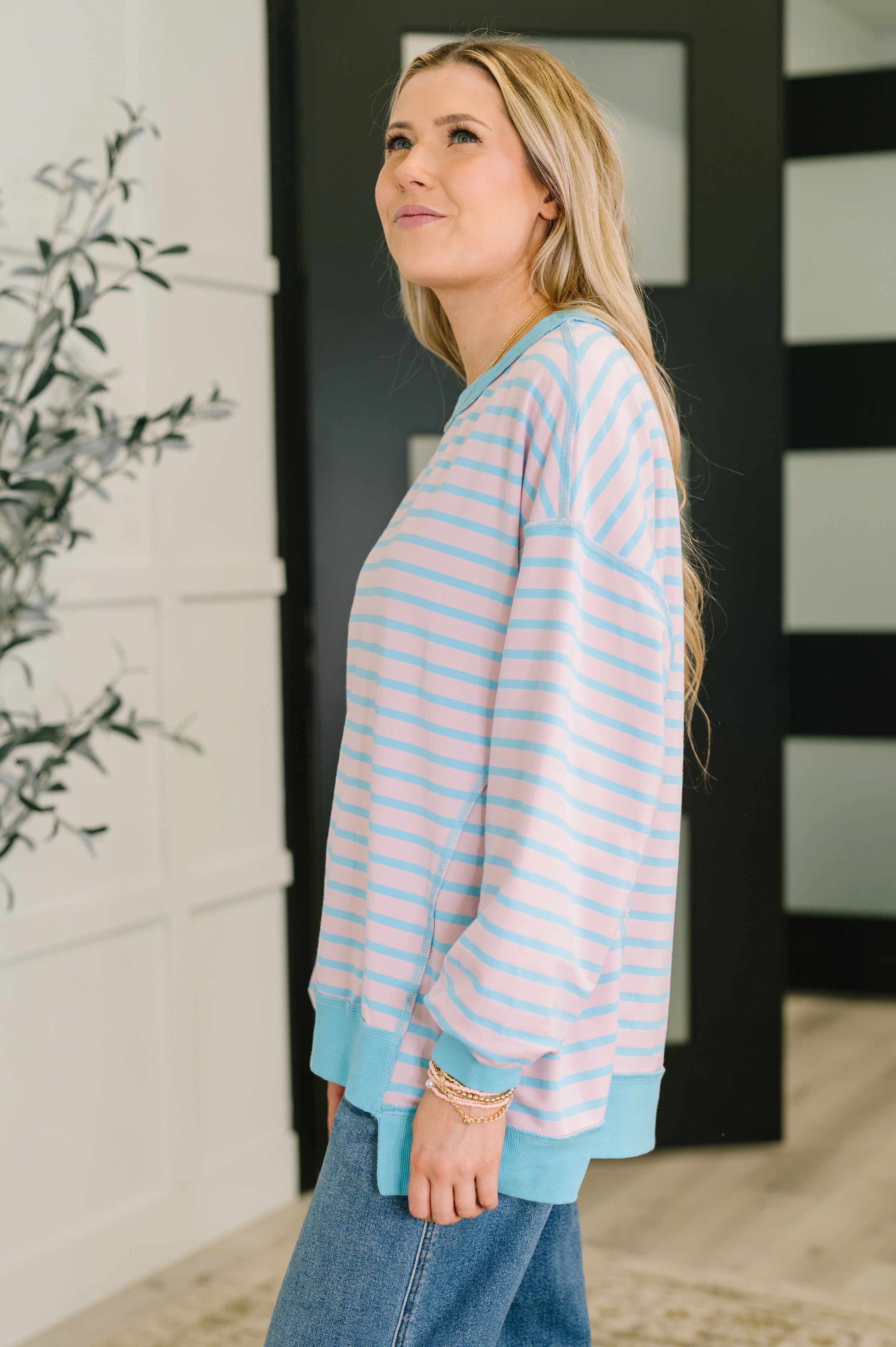 Side view of woman wearing pastel blue and pink striped drop shoulder long sleeve pullover indoors