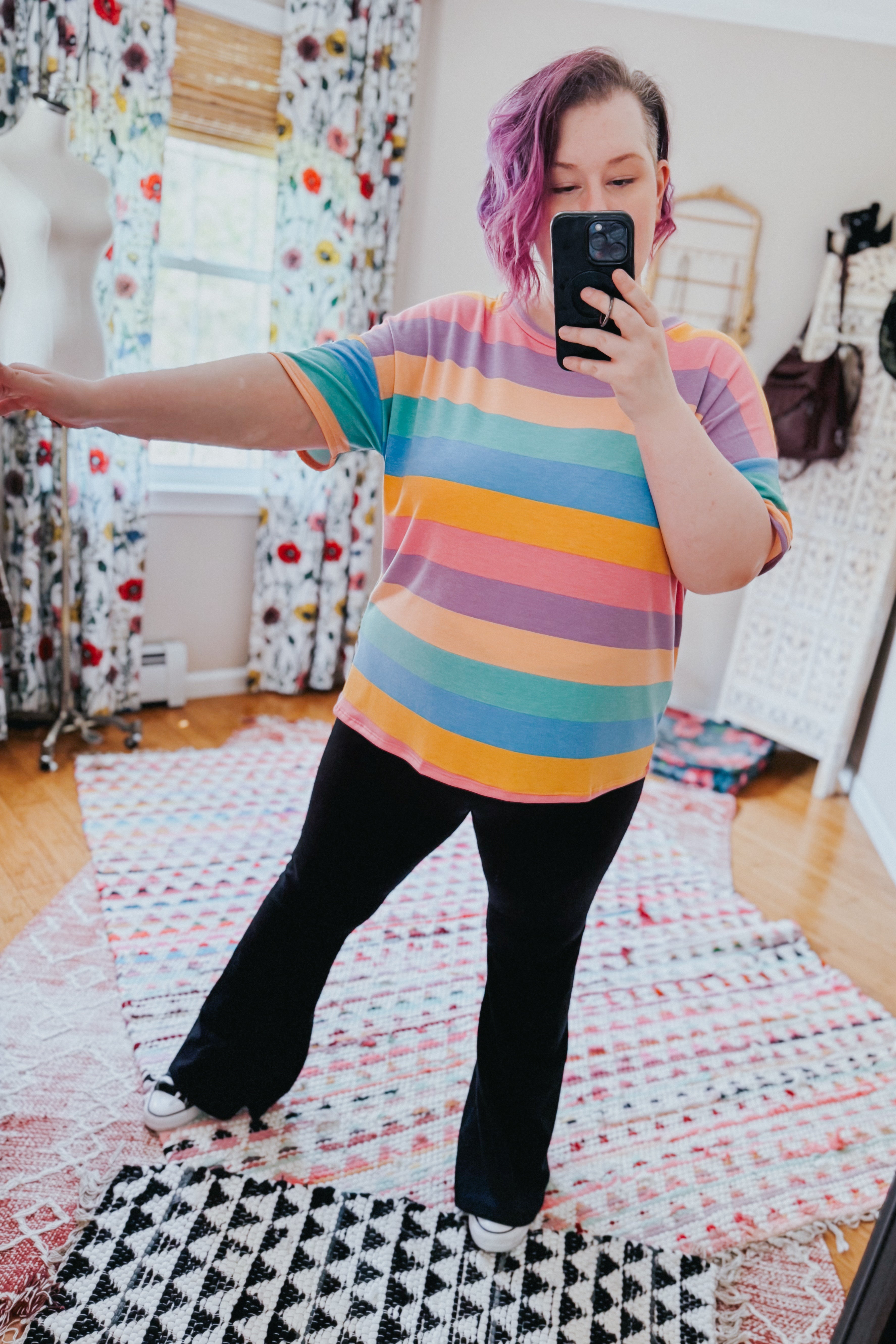Woman wearing colorful horizontal striped drop shoulder top with black pants taking selfie in bright room