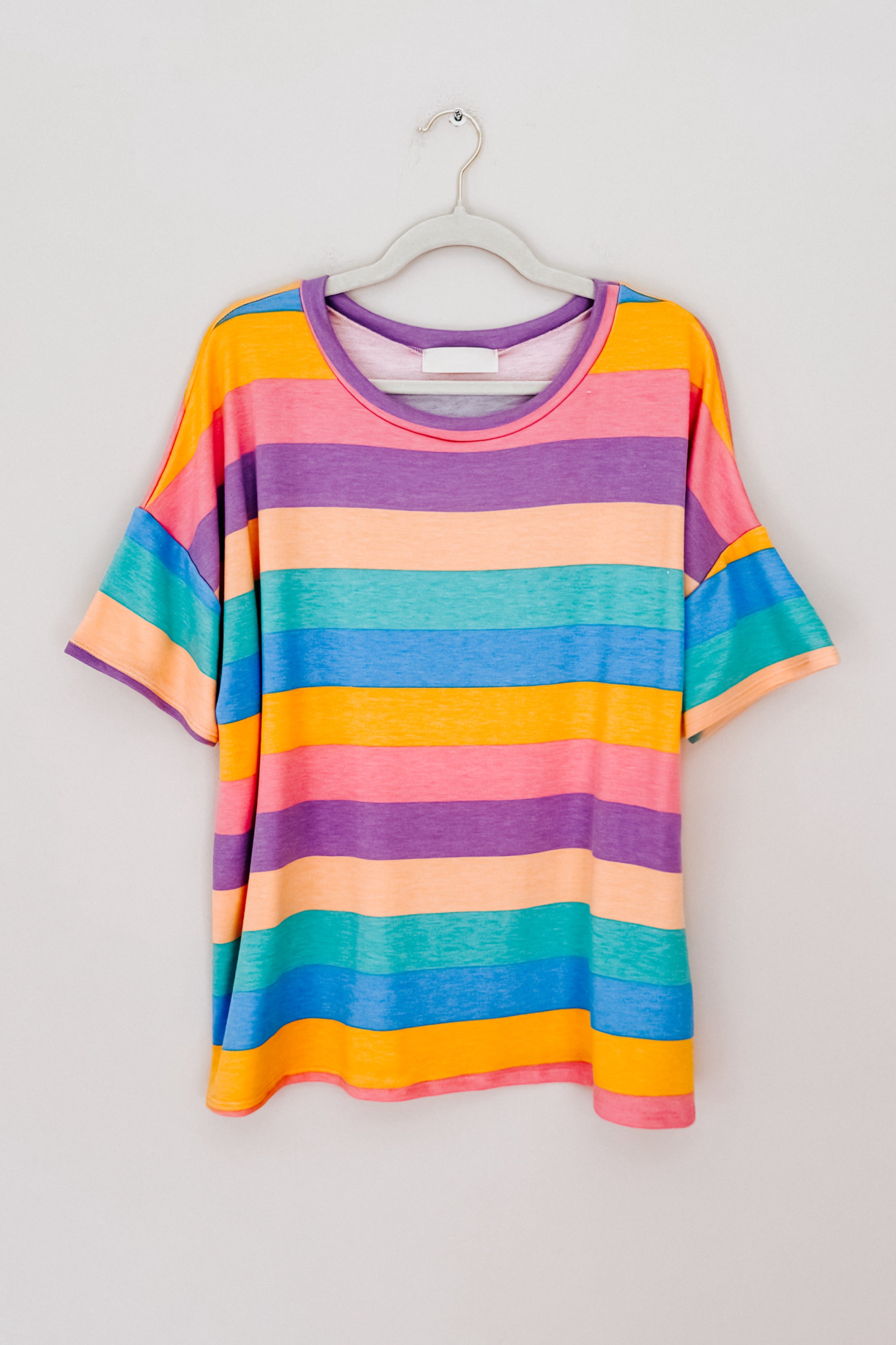 Brightly colored horizontal striped drop shoulder top hanging on white hanger against plain wall