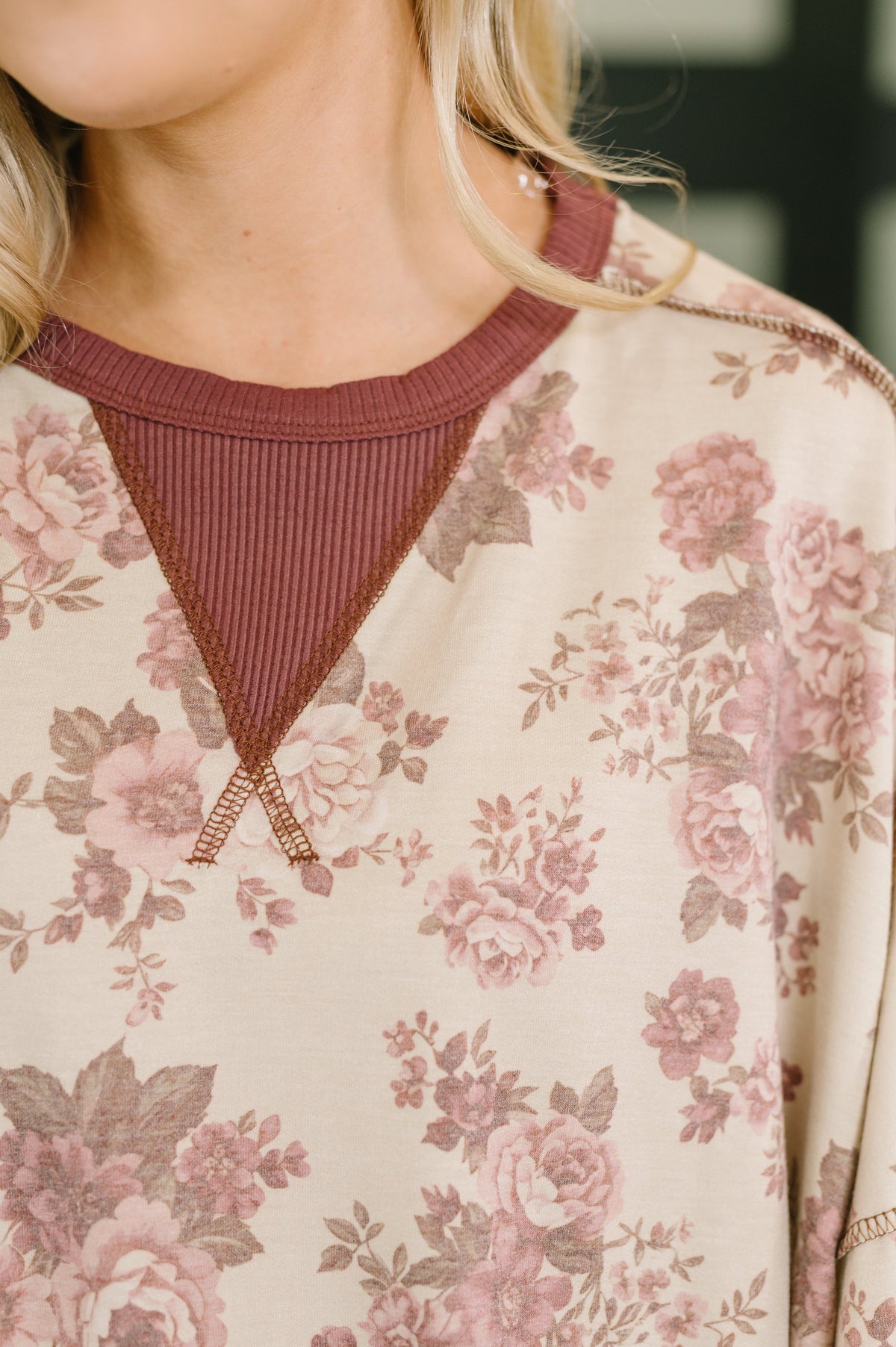 Close-up of a cream floral pullover featuring a rust ribbed V-neck inset and coordinating neckline detail