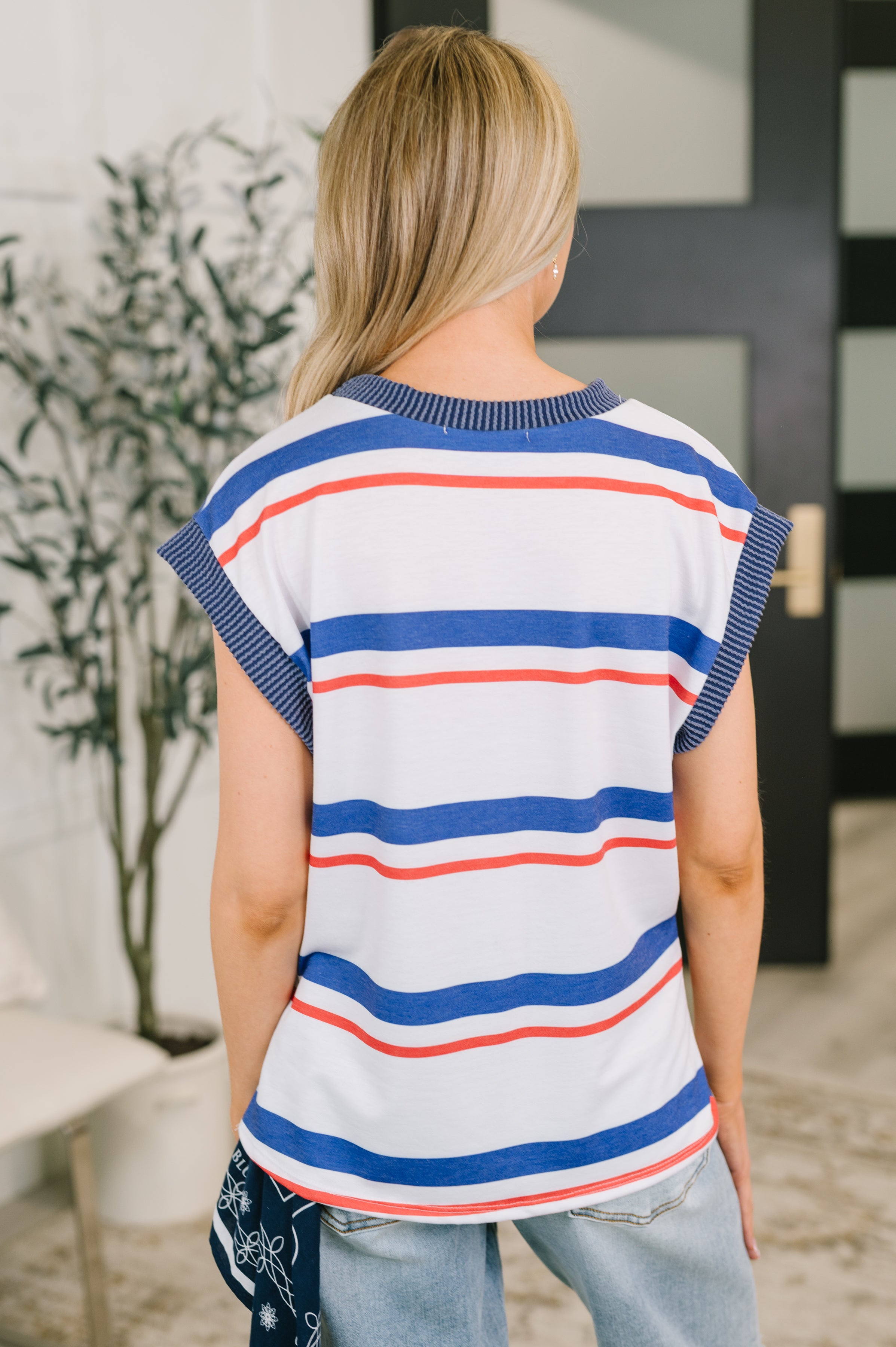 Back view of woman wearing a stretchy sleeveless striped top with blue and red bands in an eclectic indoor setting