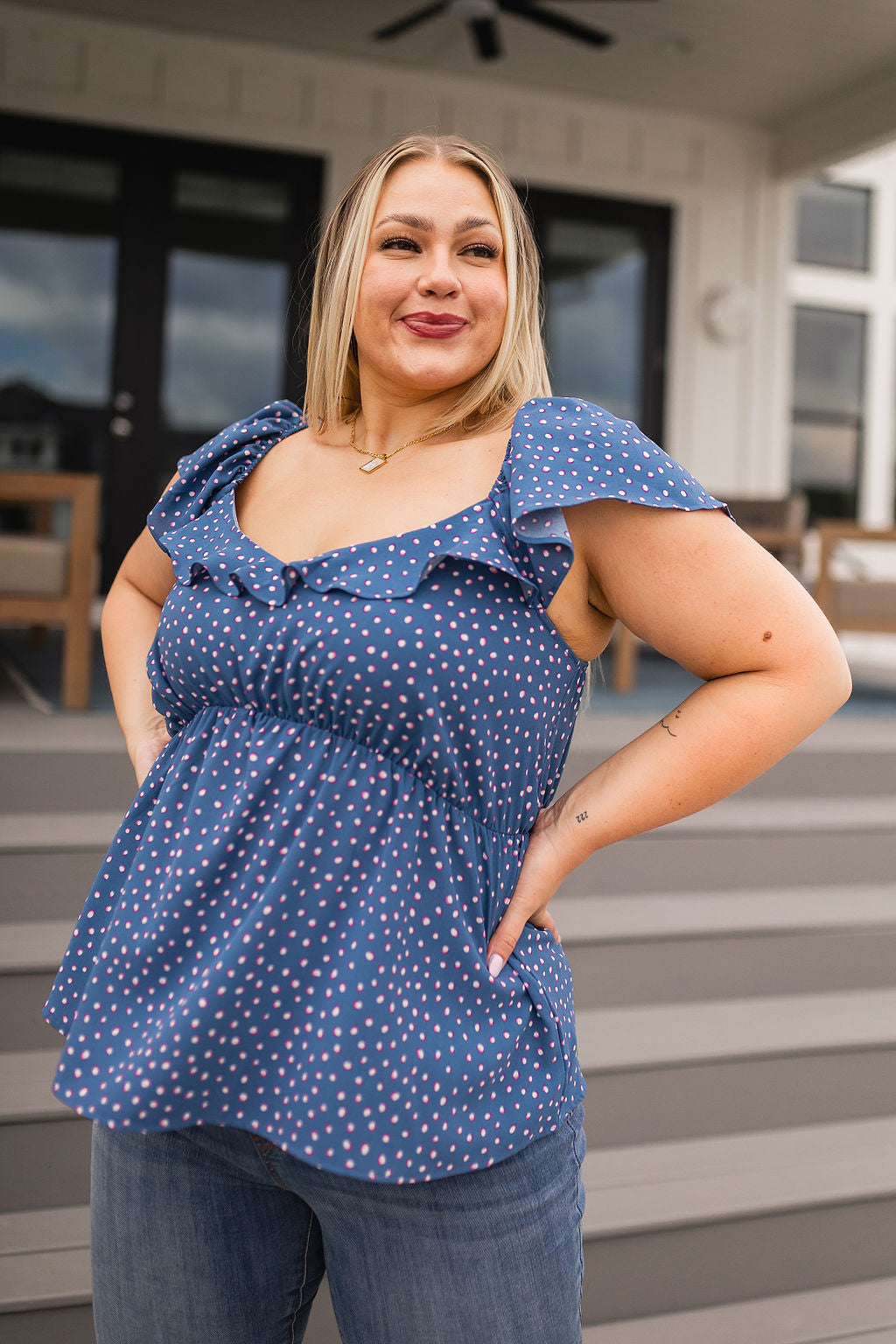Plus size woman wearing blue peplum blouse with pink polka dots and flutter sleeves standing outdoors on steps