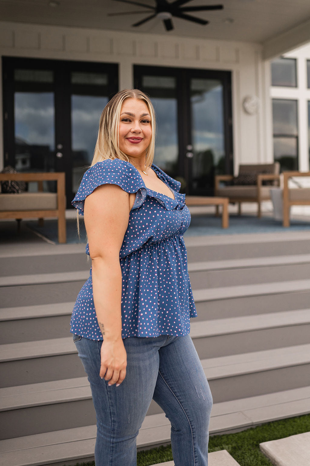 Plus size woman with blonde hair wearing blue polka dot Connect the Dots peplum blouse and jeans standing outdoors