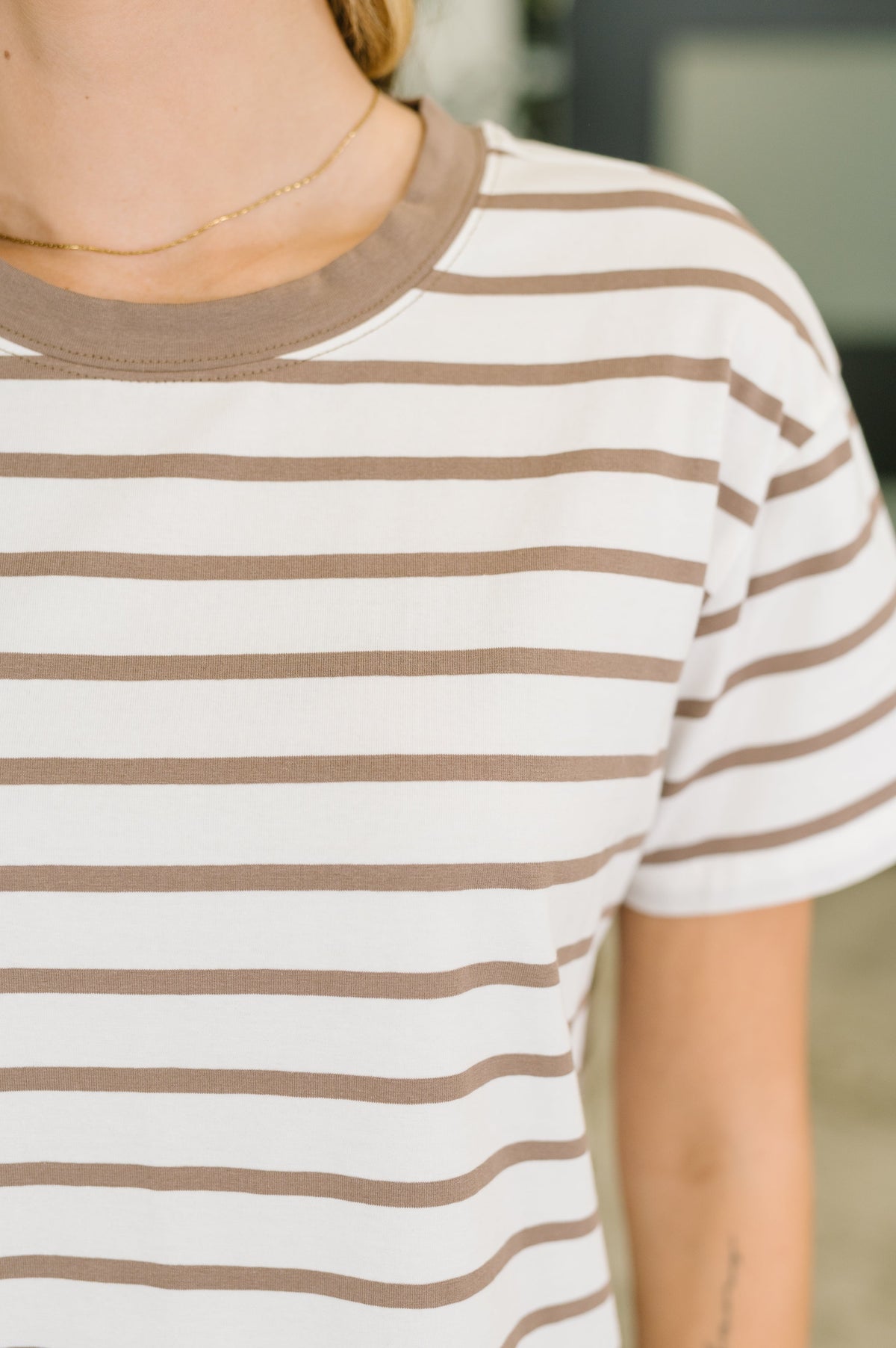 Close-up of a woman wearing a Mocha and cream striped short sleeve tee with a banded neckline and delicate gold necklace