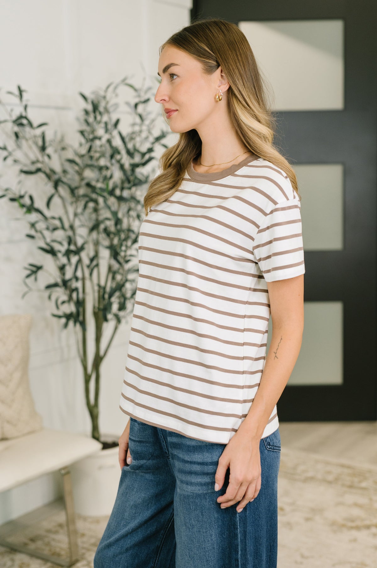 Woman wearing a Mocha and cream striped short sleeve tee with blue jeans in a modern home interior