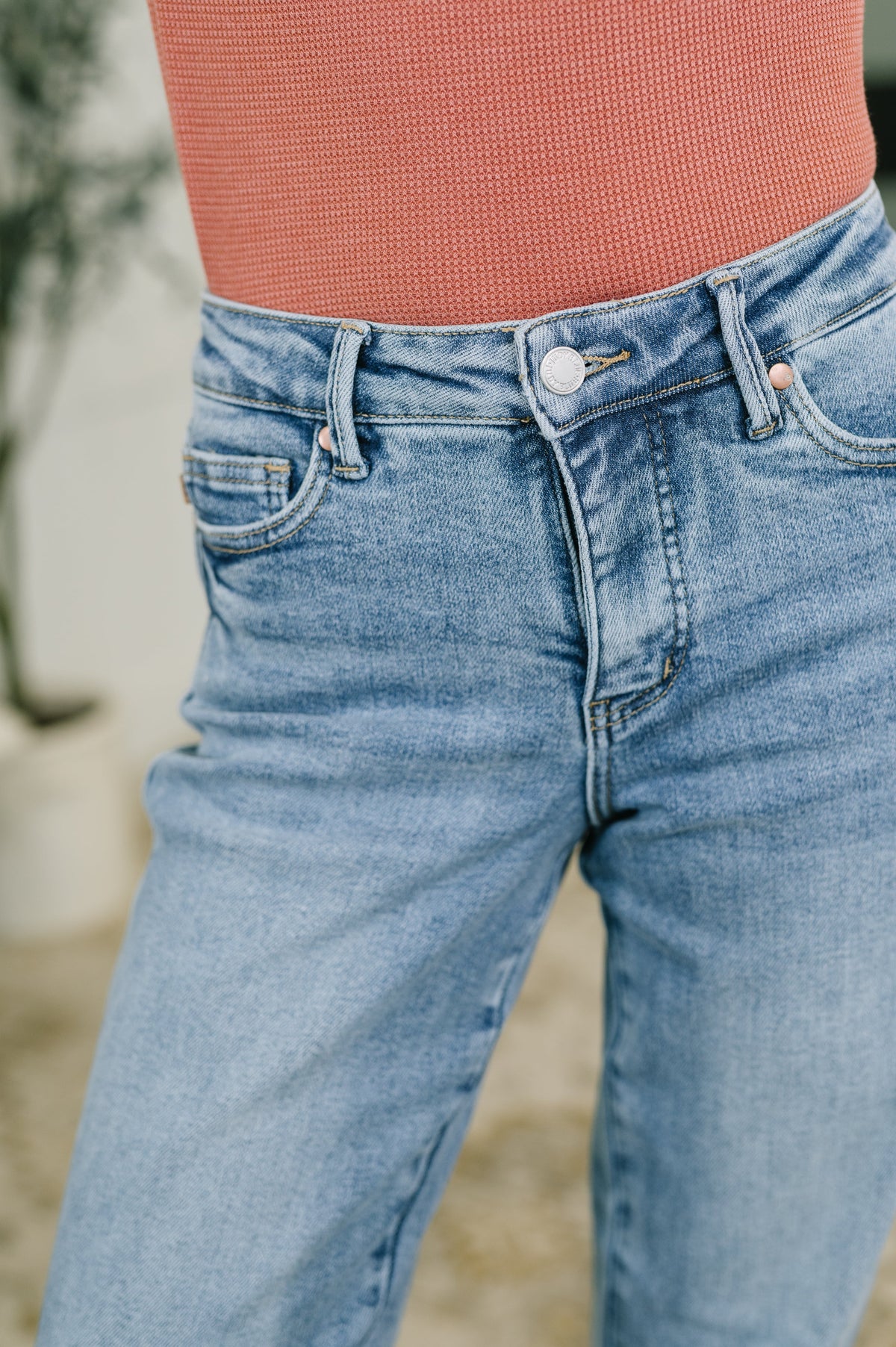 Close view of blue mid rise straight leg jeans with tummy control waistband and classic five pocket styling worn with a rust textured top