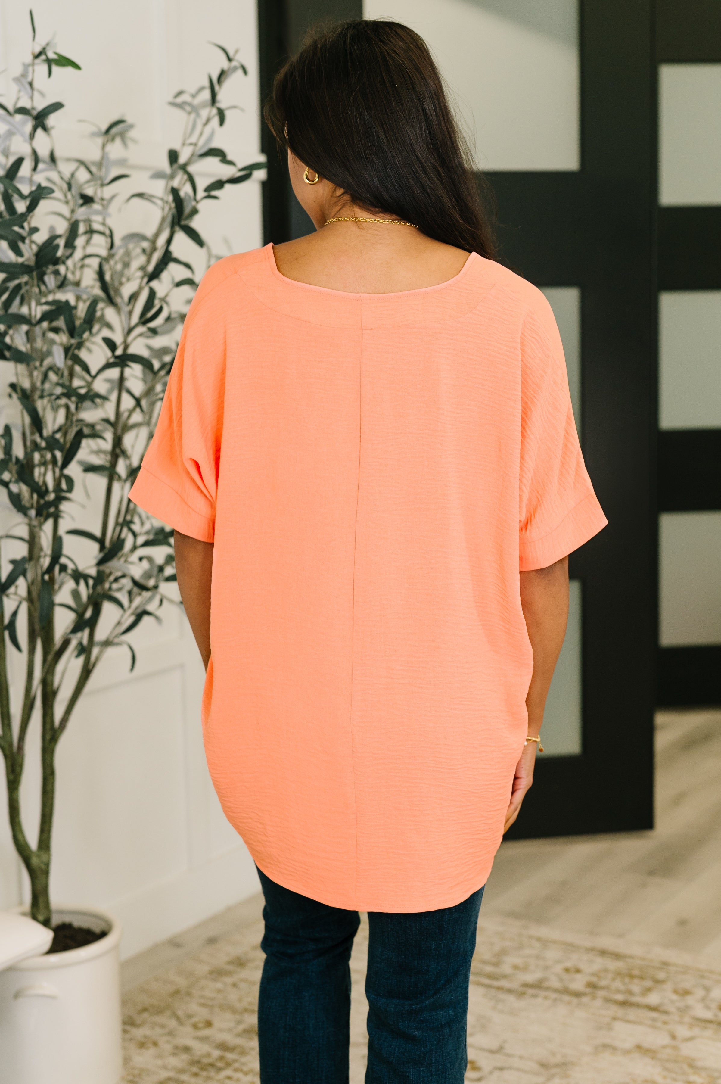 Woman seen from behind wearing coral crinkle woven short sleeve top with rolled cuffs indoors