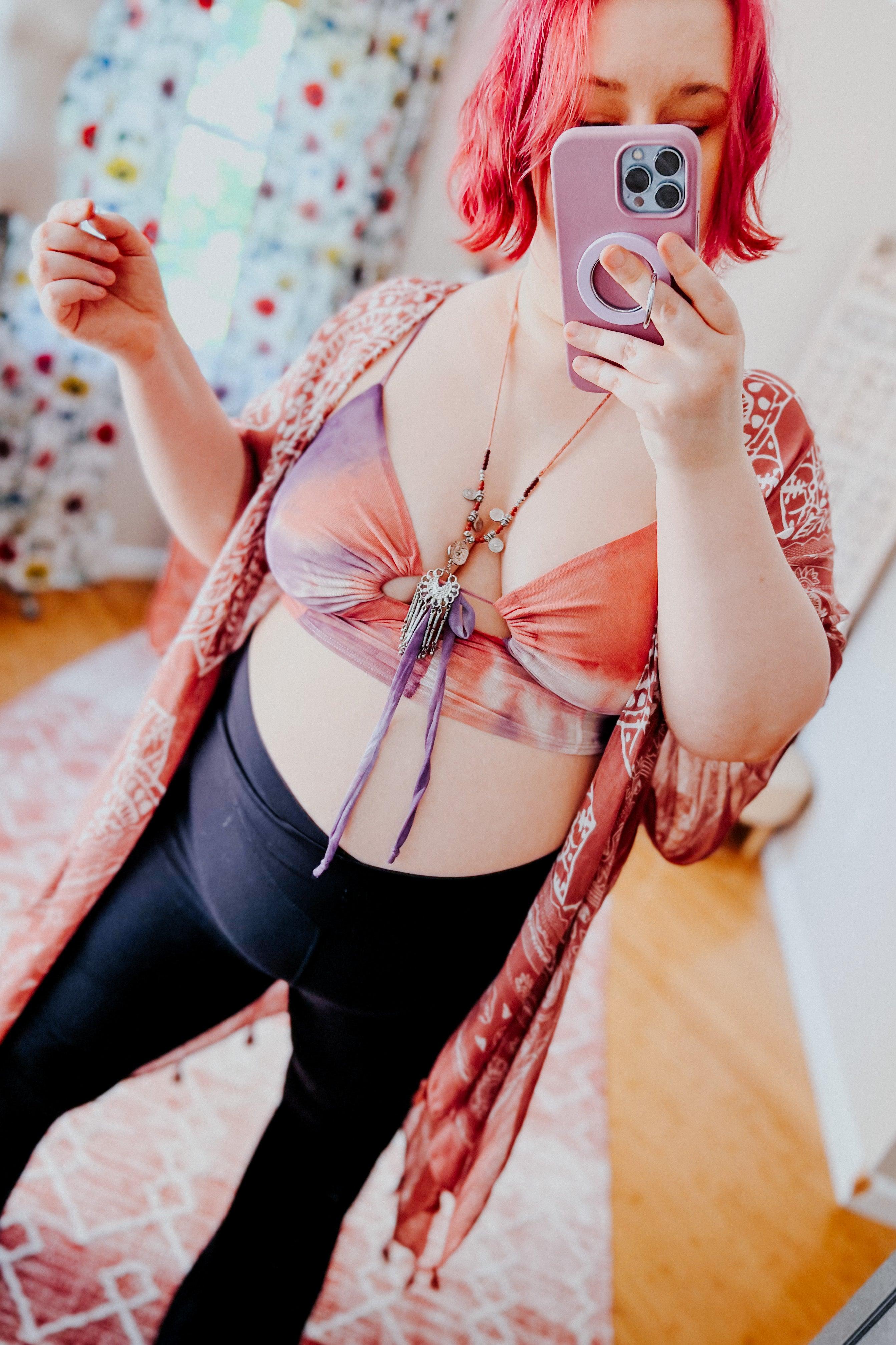 Plus size woman with short pink hair wearing tie dye mesh brami top and patterned kimono taking mirror selfie indoors