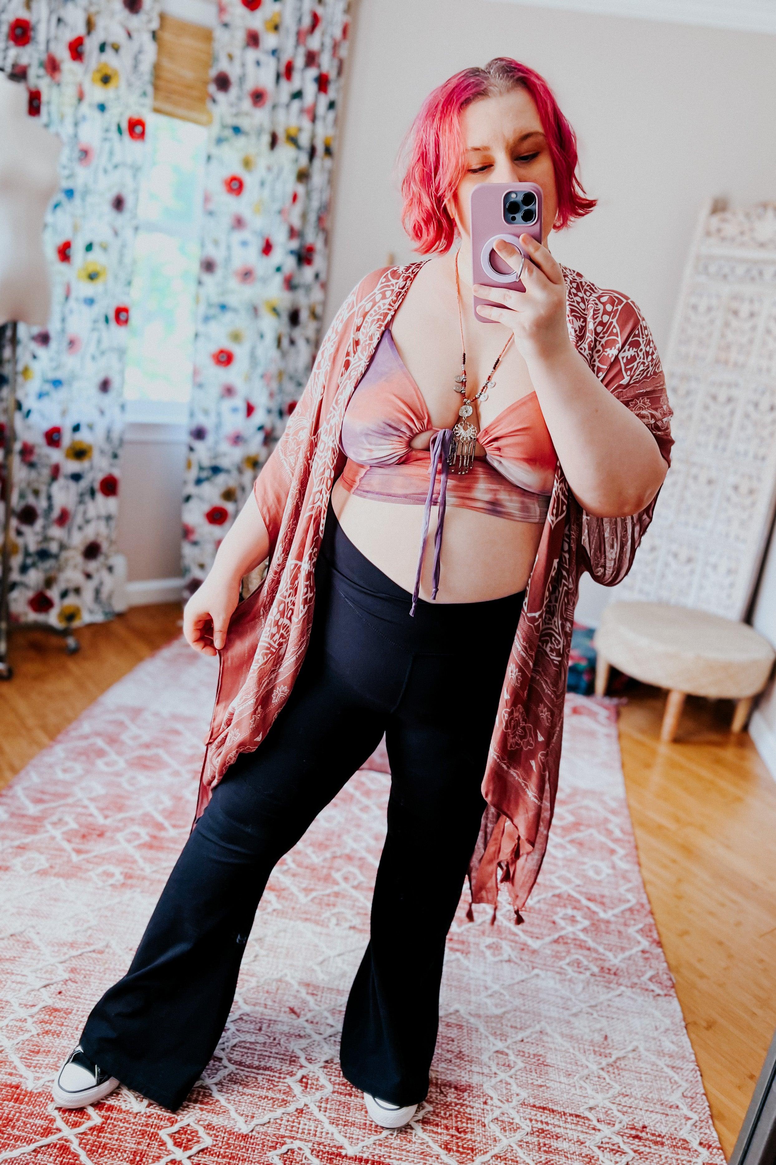 Plus size woman with pink hair wearing tie dye brami top and patterned kimono taking mirror selfie indoors