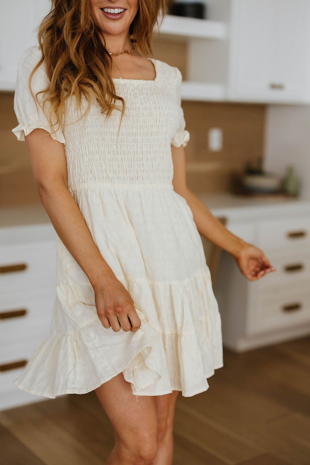 Woman wearing ivory square neck dress with puff sleeves and gathered bodice in cozy indoor setting