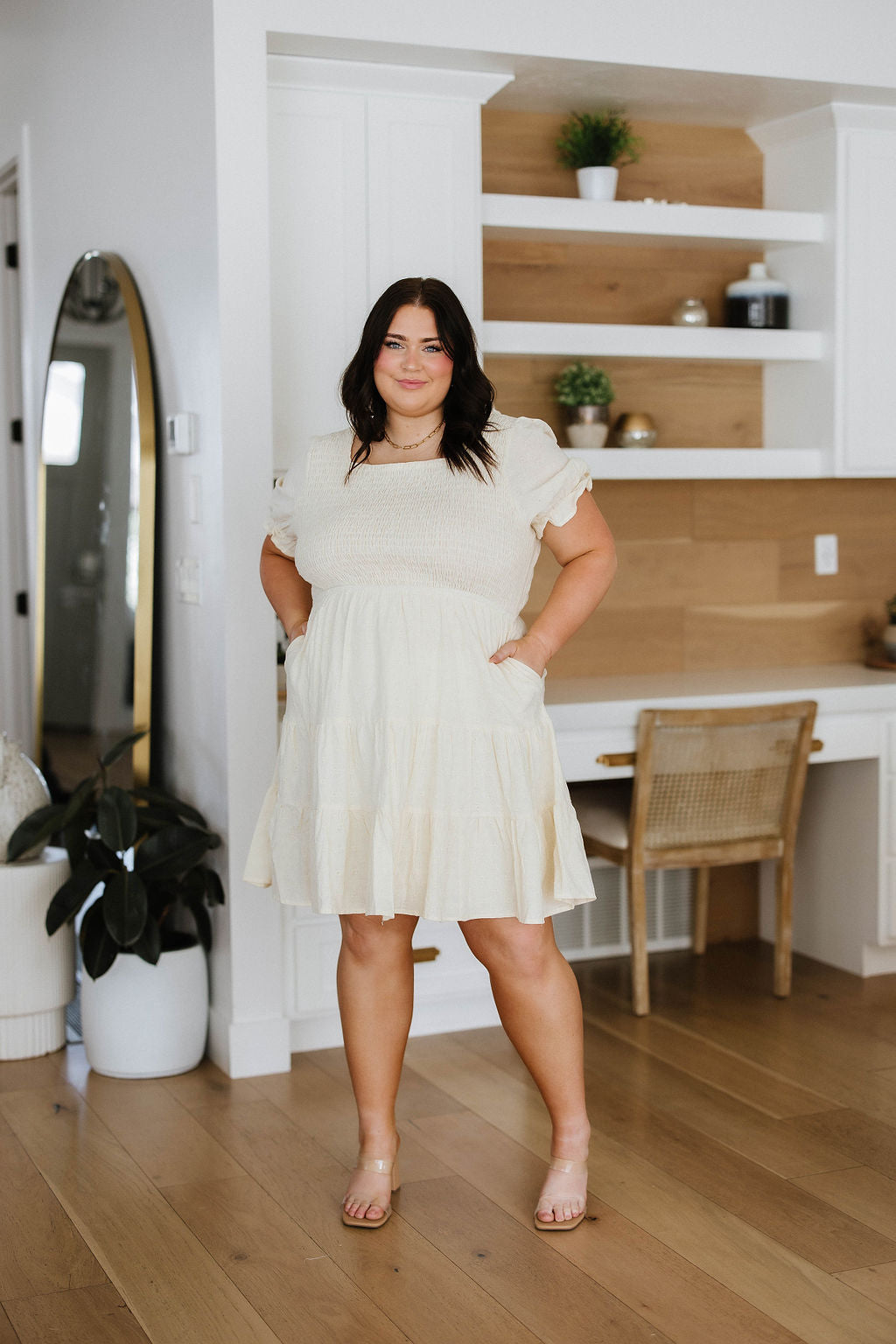 Woman wearing ivory square neck dress with puff sleeves and tiered skirt standing in modern room