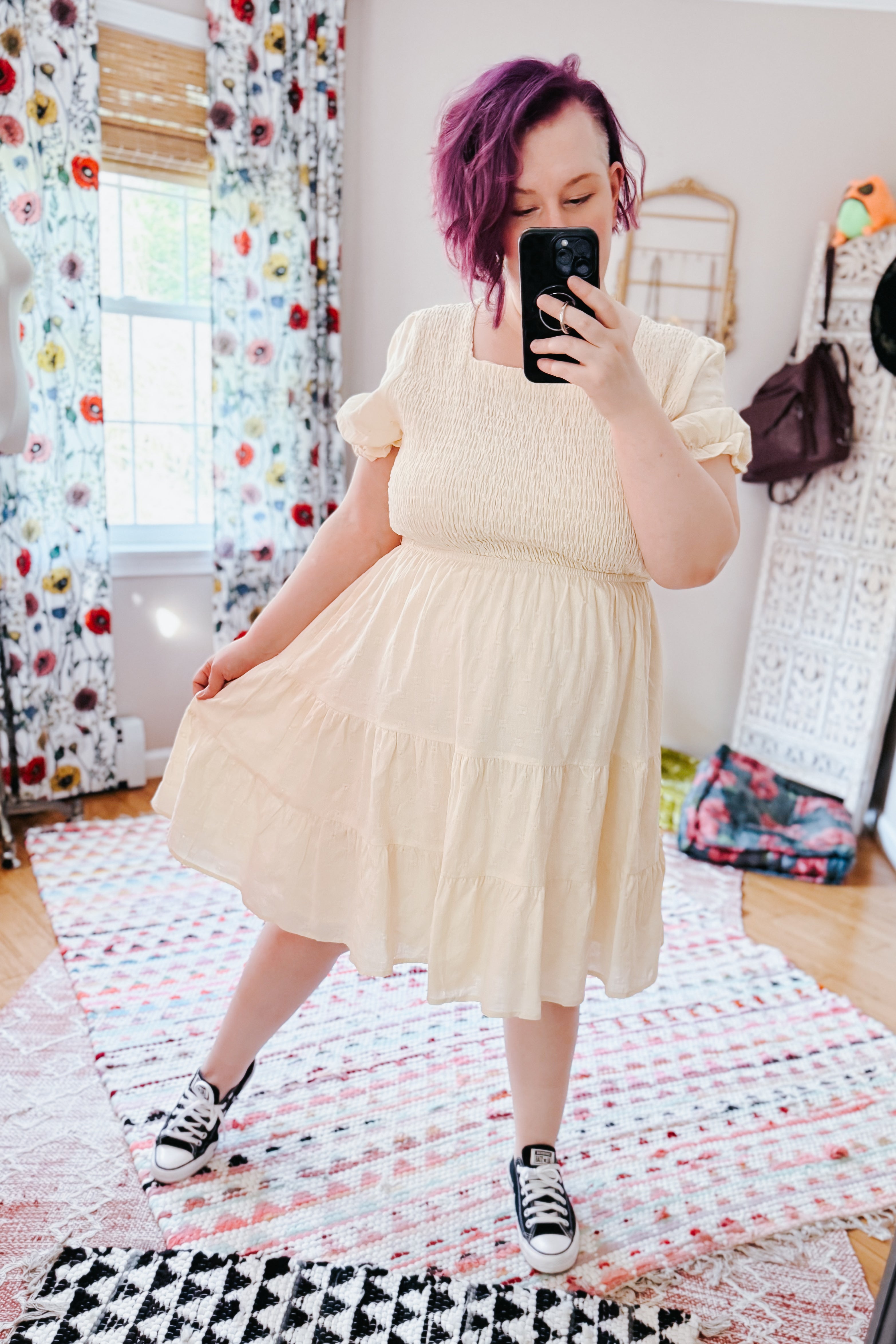 Woman with purple hair wearing an ivory square neck dress with puff sleeves and sneakers in a bright eclectic room