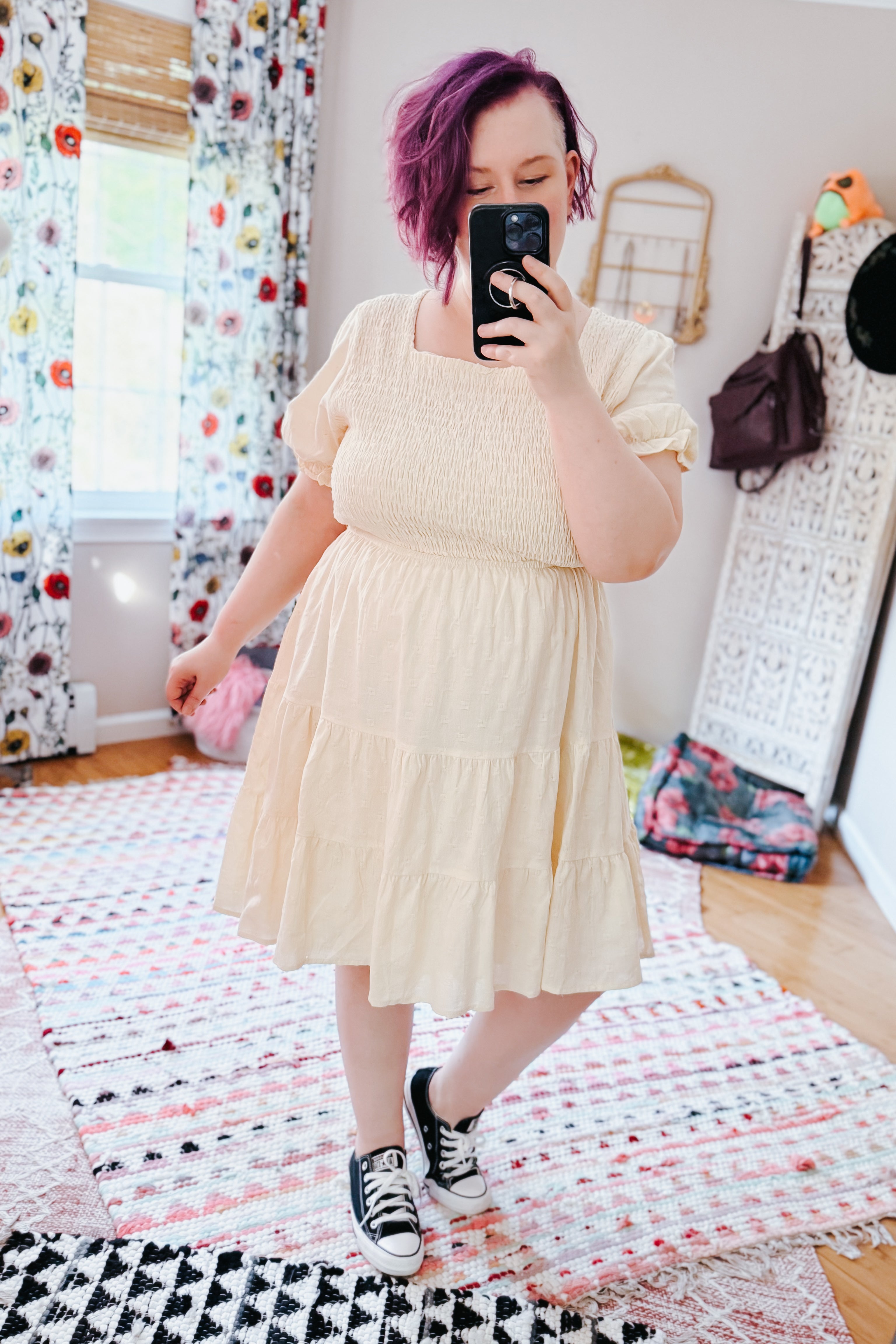 Woman with purple hair wearing an ivory square neck dress with puff sleeves and sneakers in a cozy eclectic room
