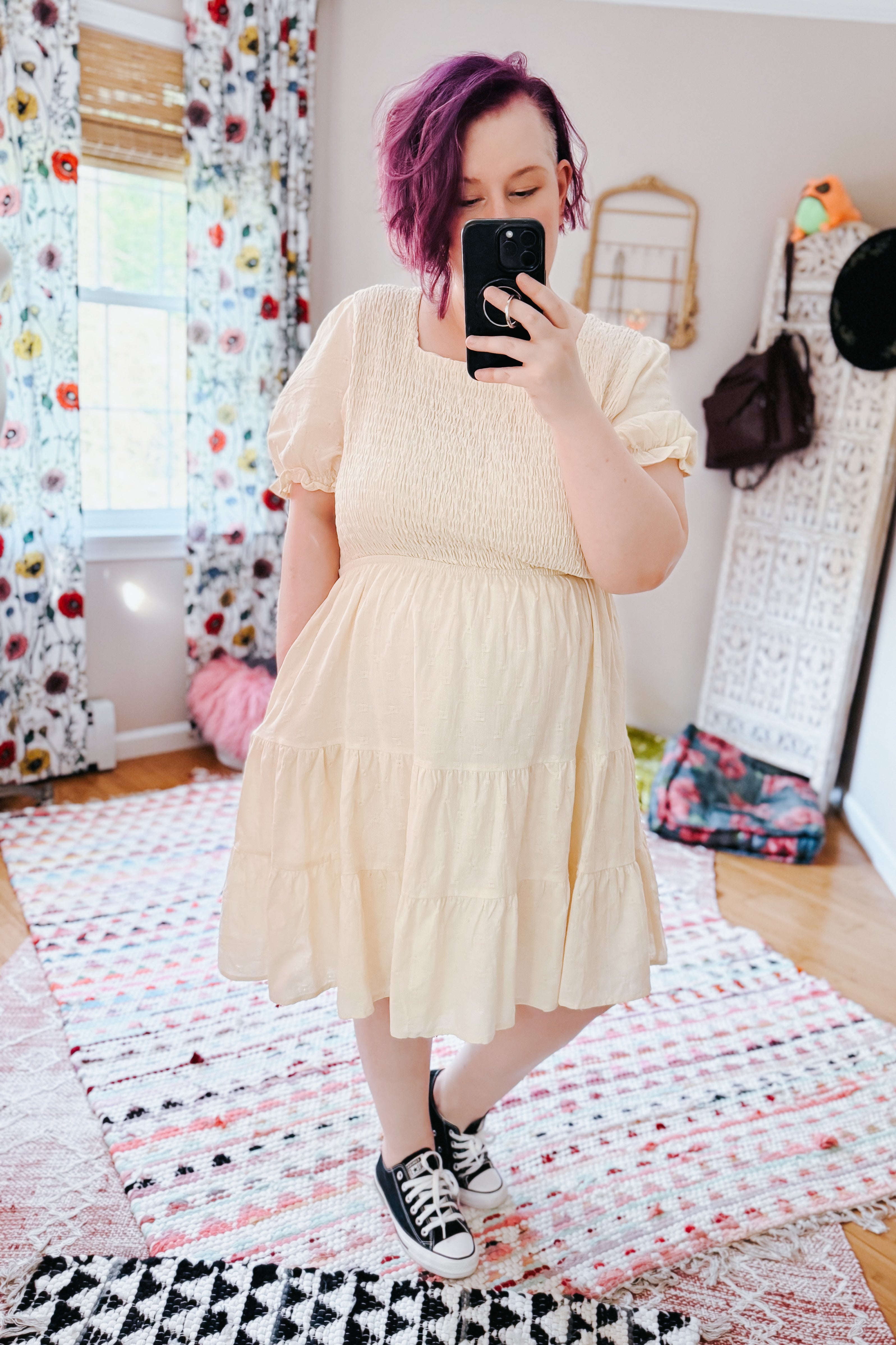 Woman with purple hair wearing an ivory smocked square neck dress with puff sleeves and sneakers in an eclectic room