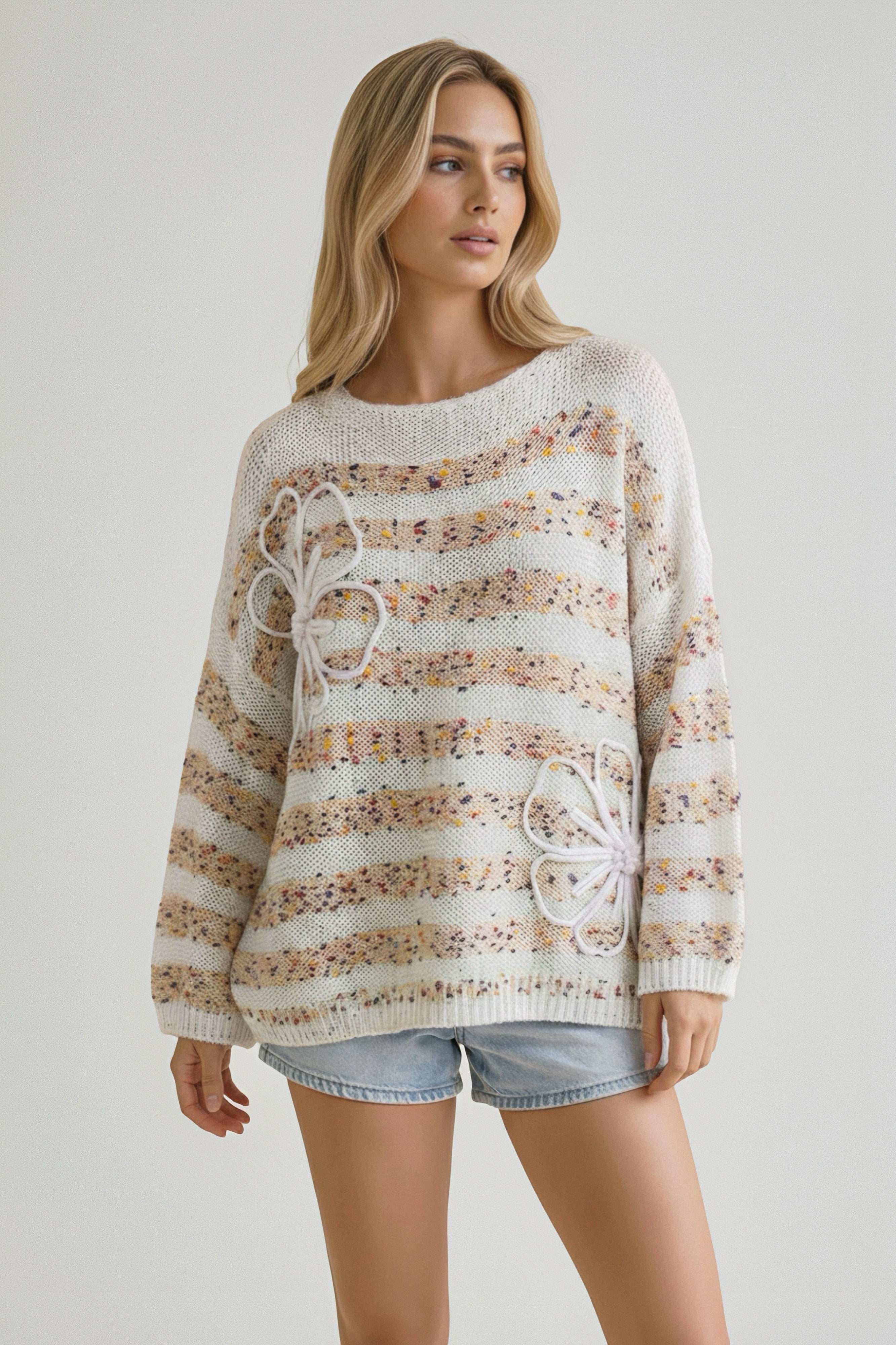 Woman wearing a beige striped knit sweater with raised floral accents paired with light denim shorts