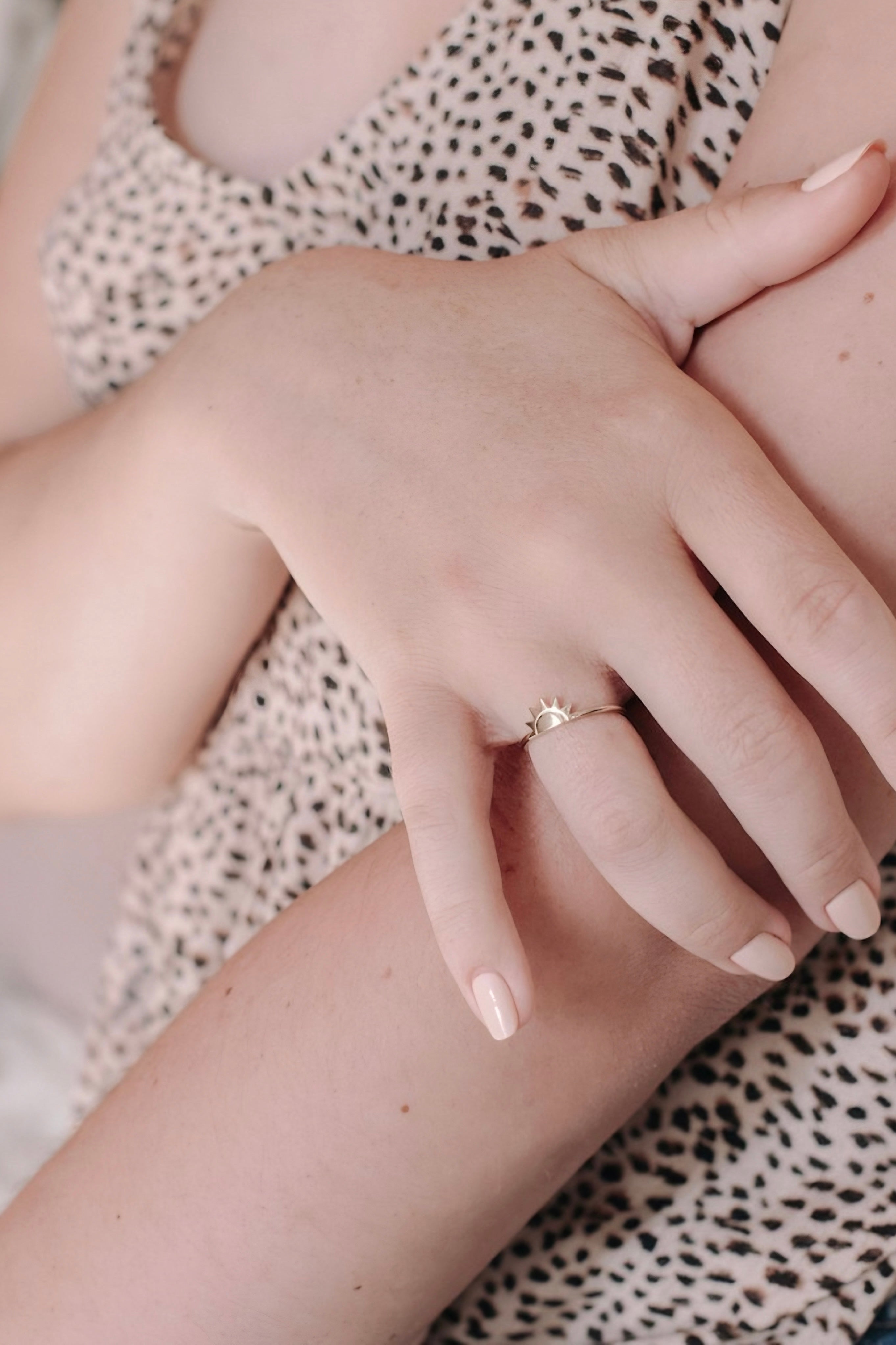 Close-up of hand wearing gold sun-inspired ring duo on a neutral patterned fabric background