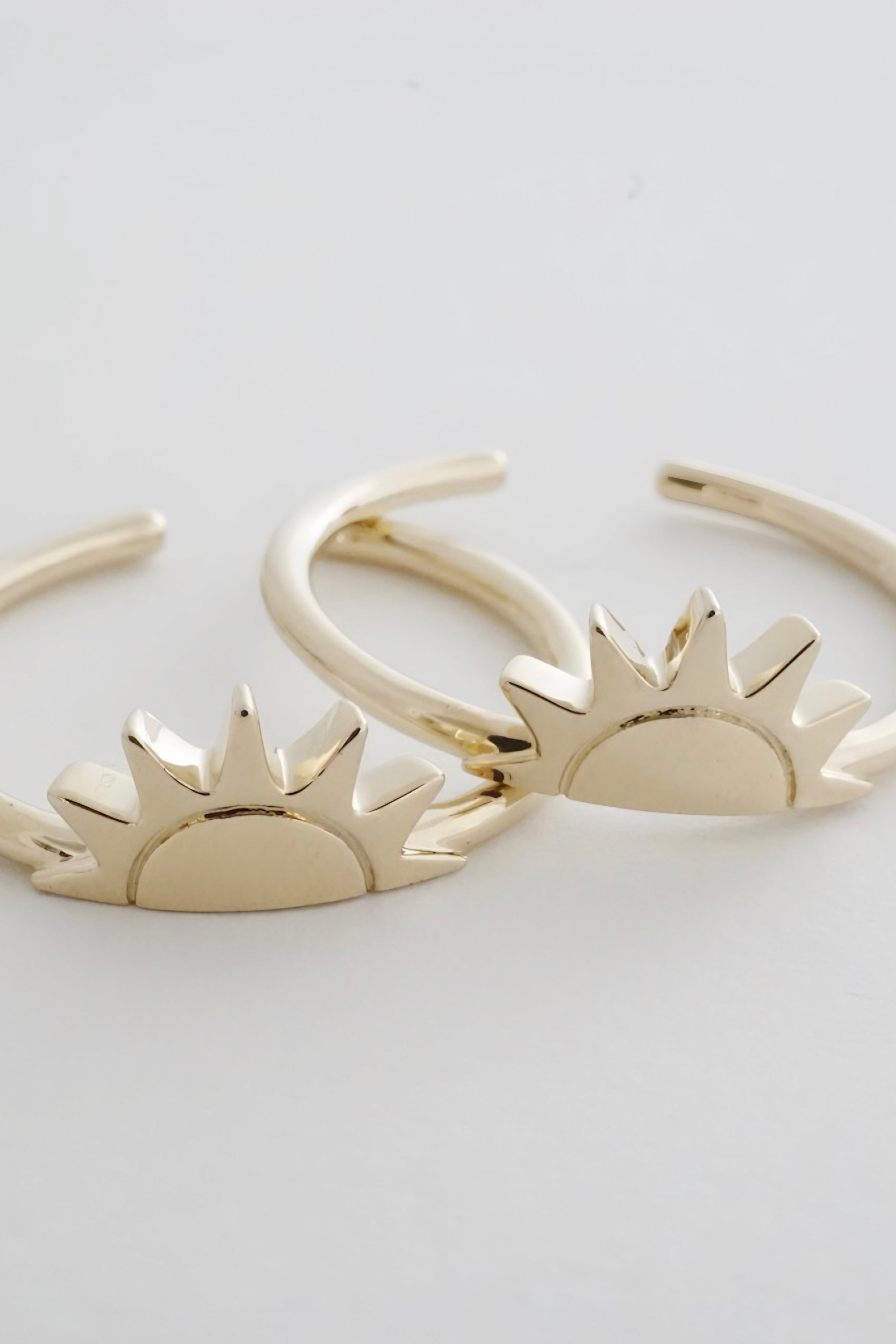 Pair of gold rings featuring polished sunburst designs on a plain white background with soft lighting