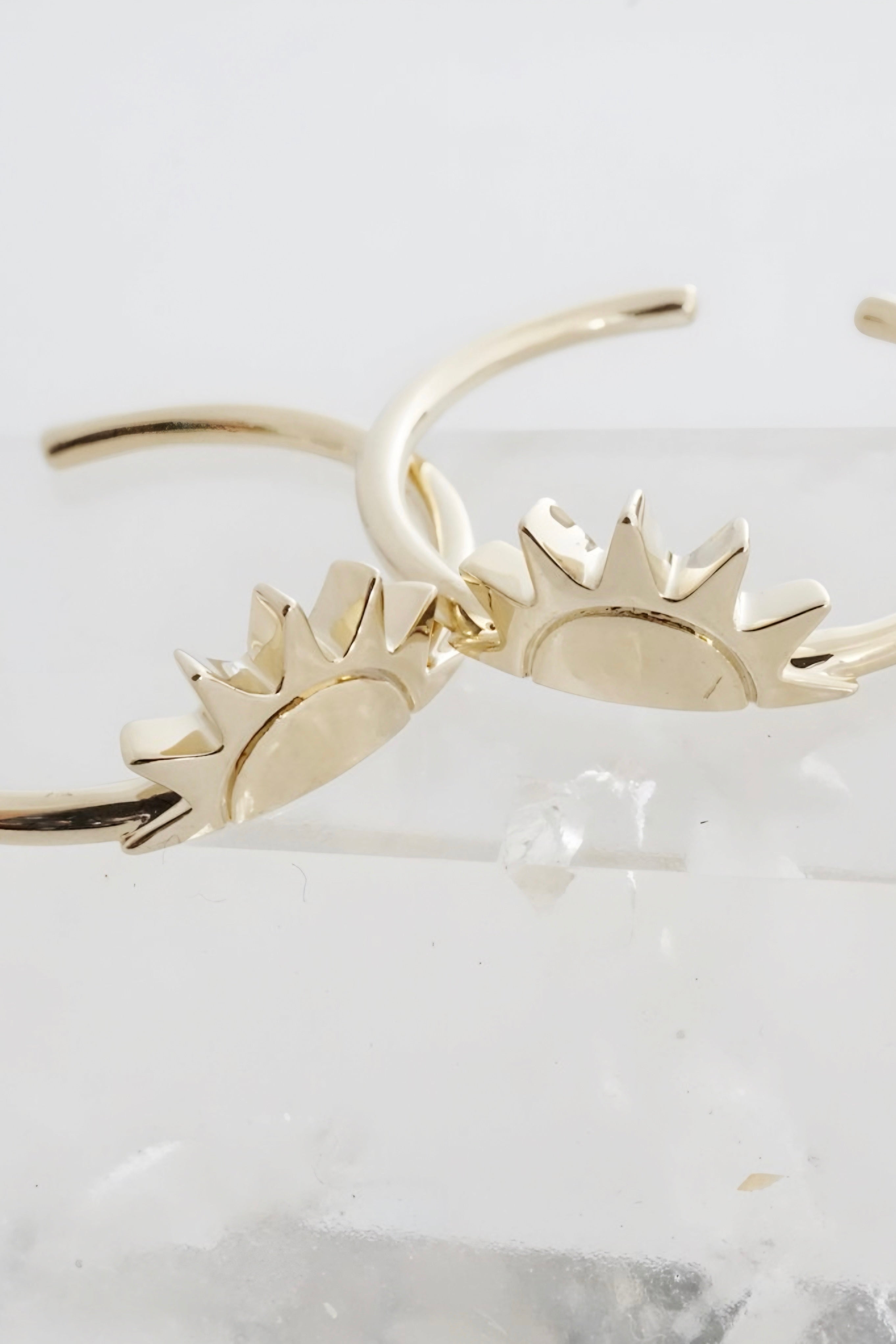 Close-up of two gold rings with rising sun design displayed on clear acrylic block with soft lighting
