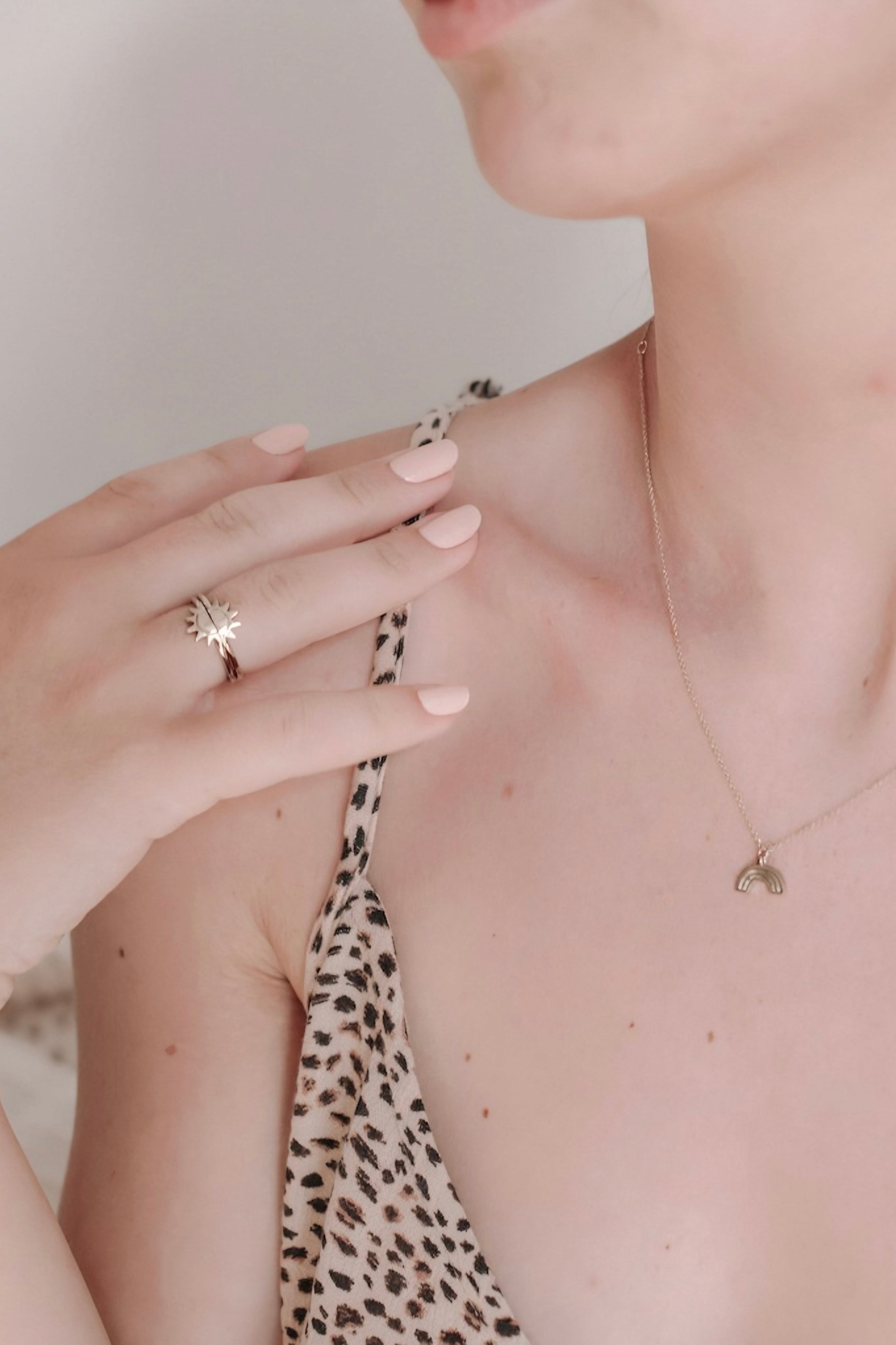 Close-up of hand wearing gold sunburst ring duo with leopard print strap and delicate gold necklace on fair skin