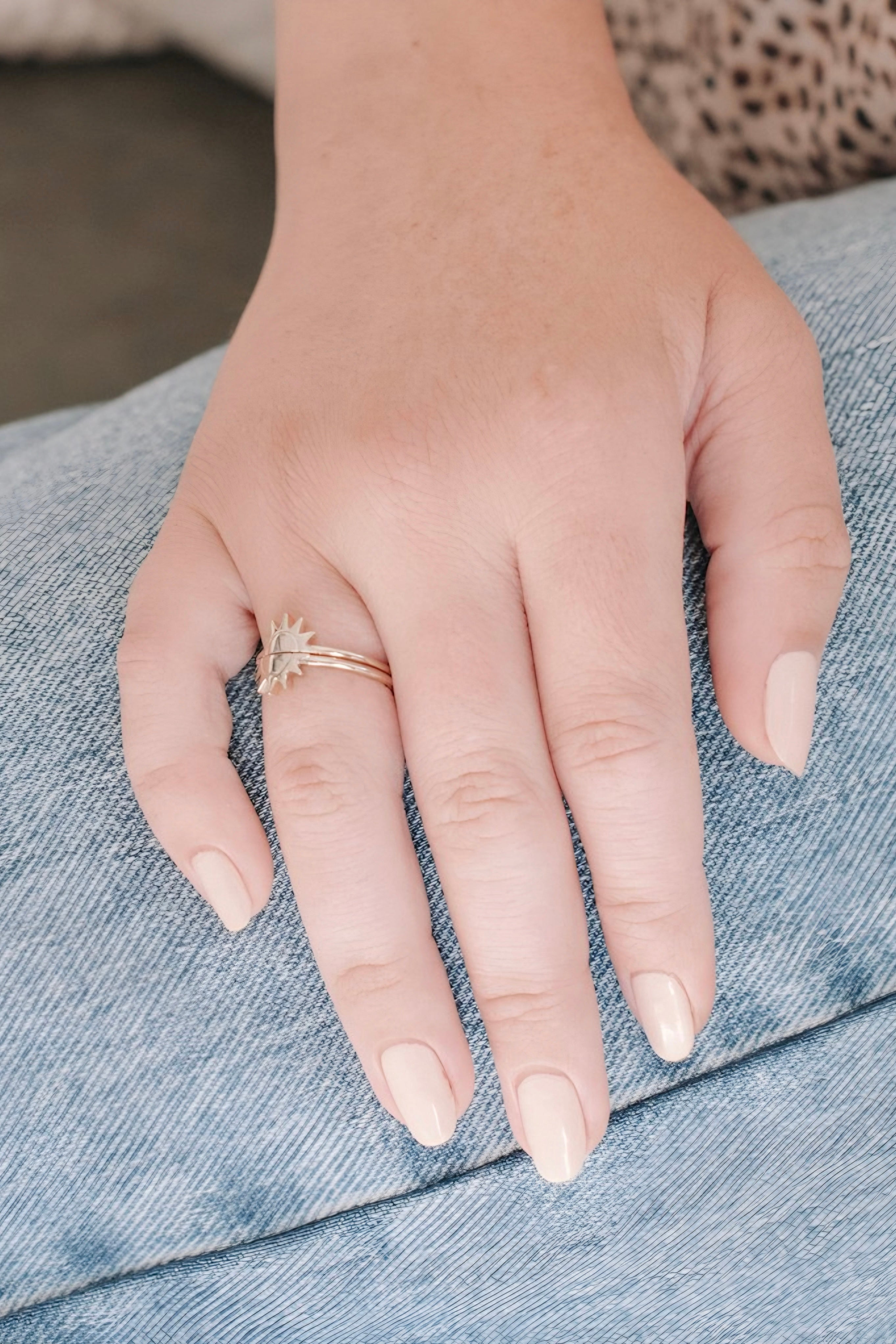Hand wearing two delicate gold rings with sun and starburst motifs resting on denim fabric background