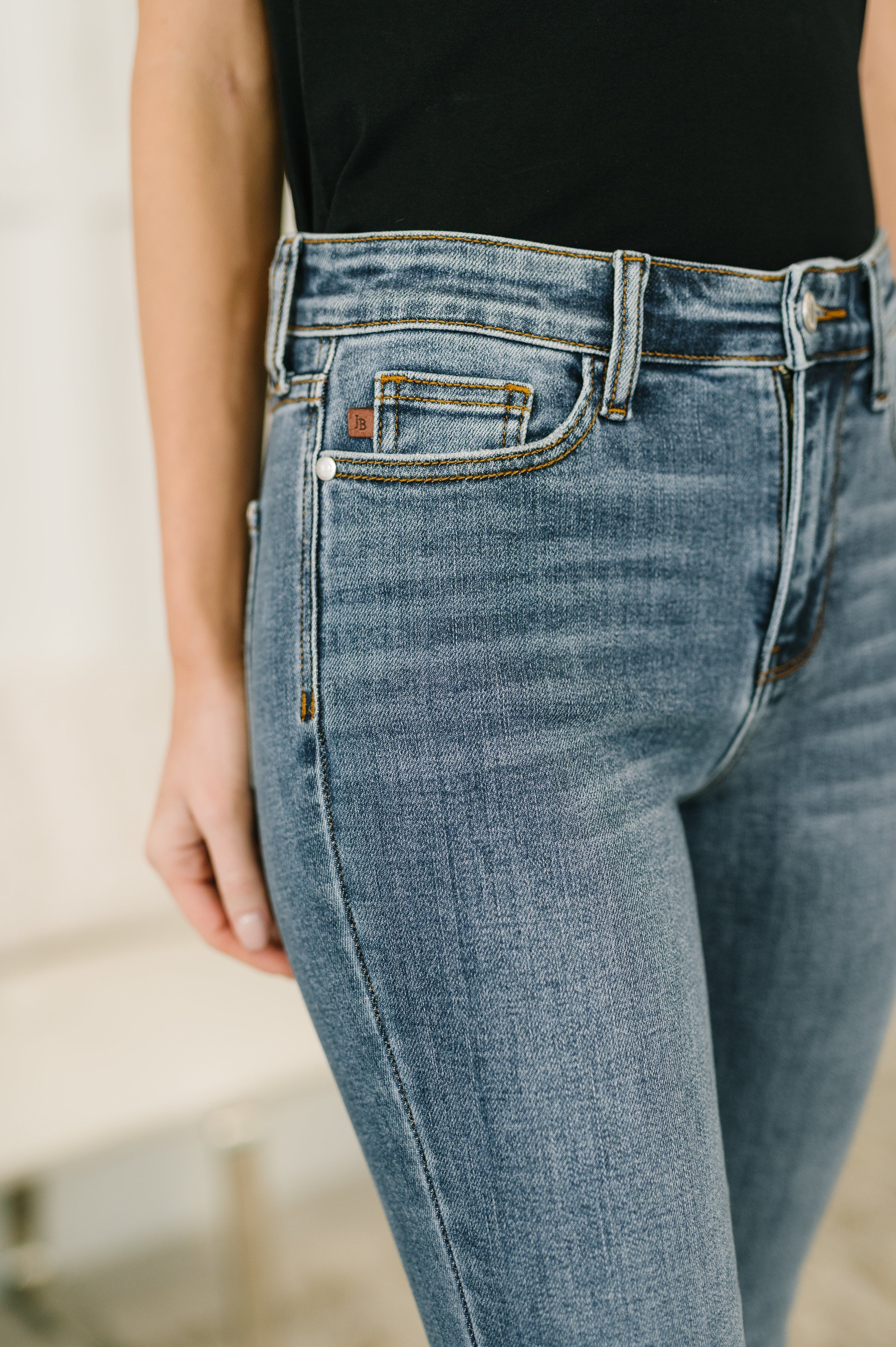 Close-up of blue denim jeans with a mid-rise waist worn with a black fitted top and visible front pocket details