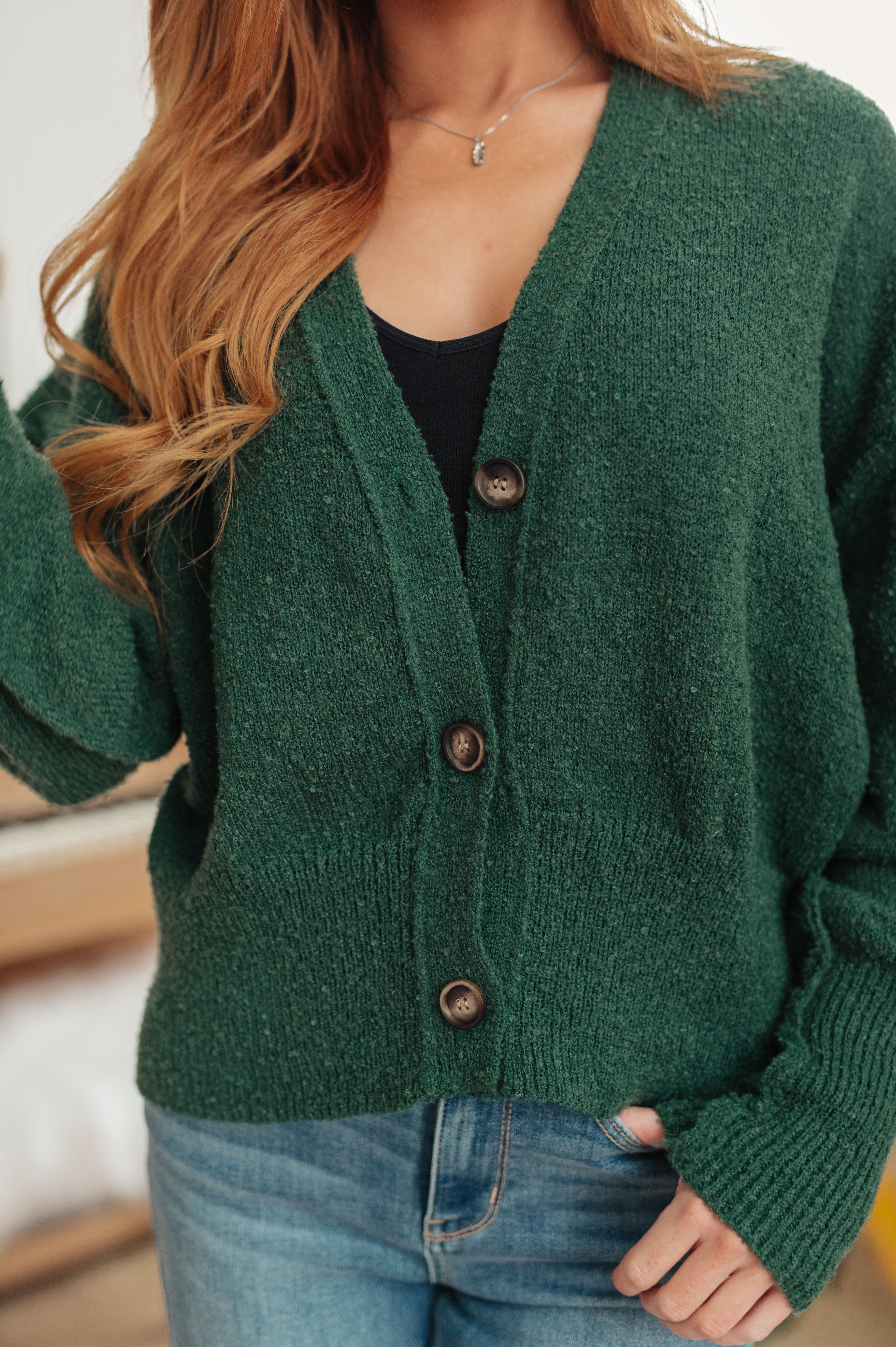 Close-up of woman wearing a deep green textured cardigan with large buttons over a black top and blue jeans