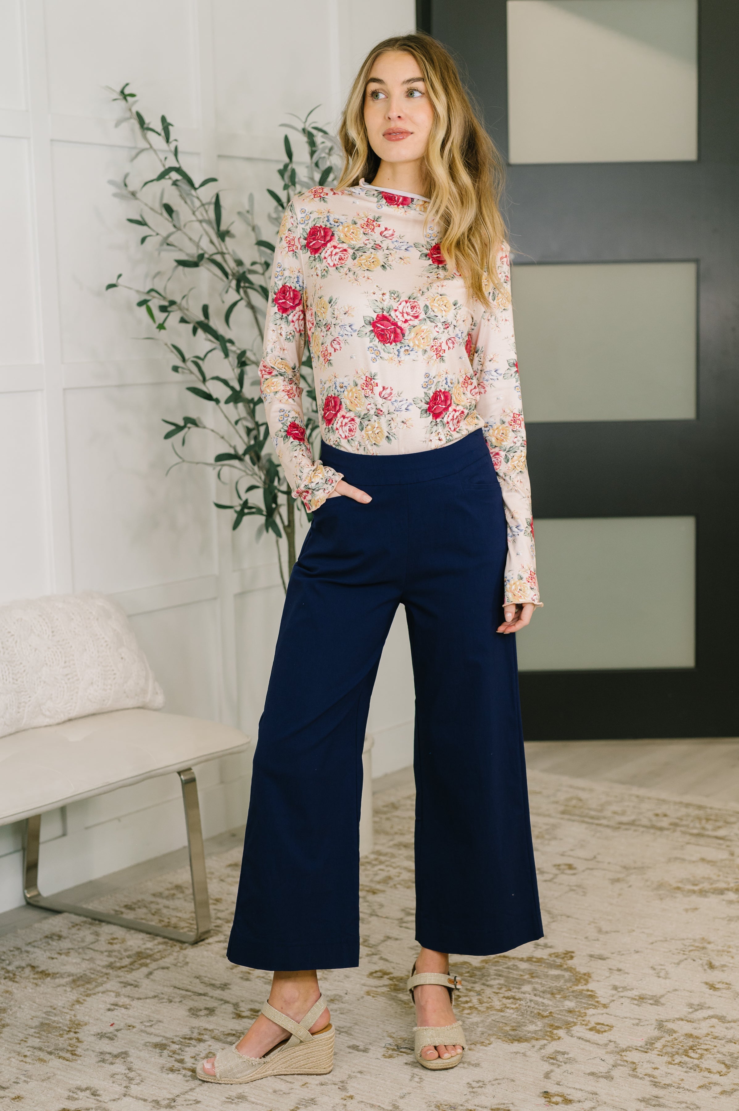 Woman wearing floral long-sleeve top with pink and red flowers paired with wide-leg navy pants and beige sandals