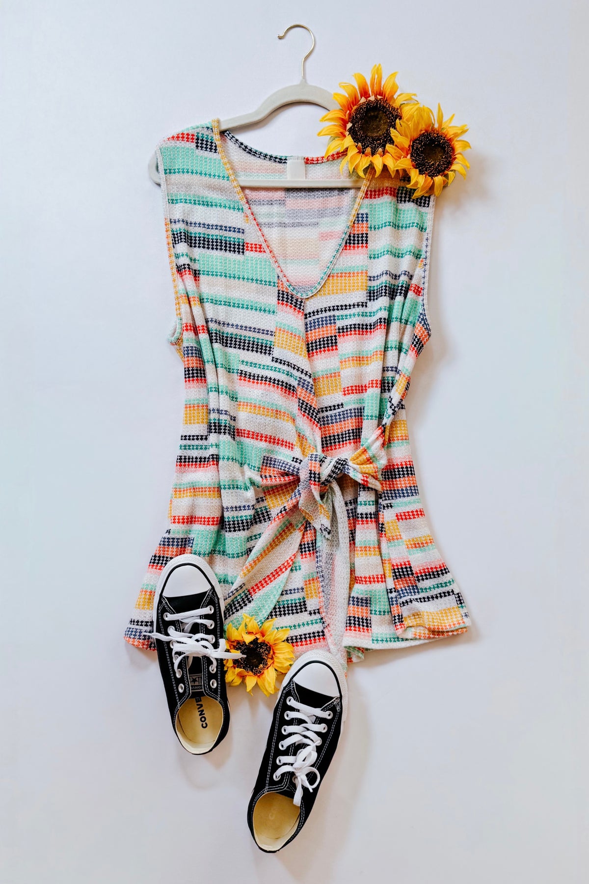 Blue multicolor plaid sweater knit V-neck tank with faux wrap tie styled on a hanger with sunflowers and black sneakers