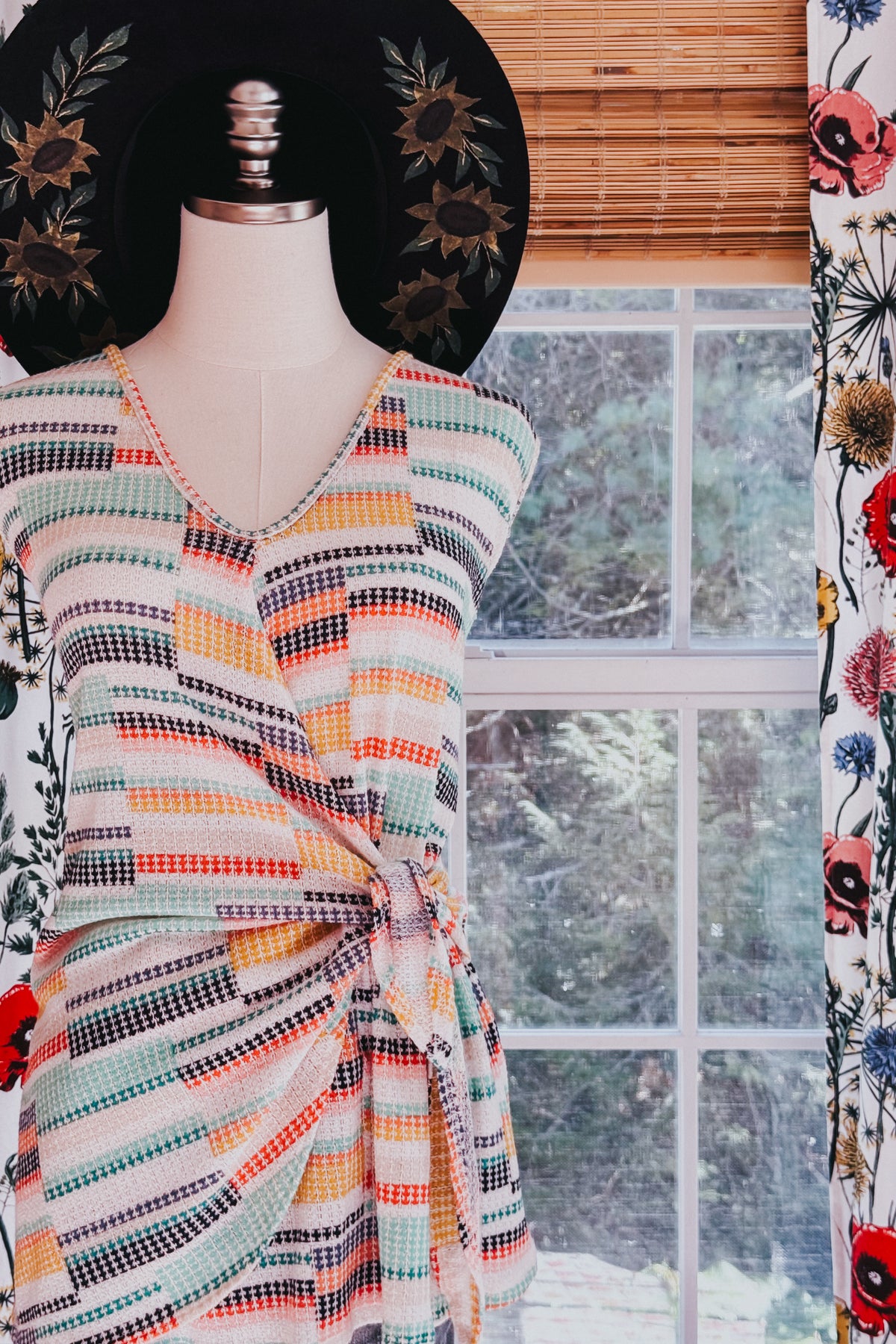Mannequin wearing a colorful striped V-neck faux wrap knit tank with blue, orange, coral, and black accents indoors