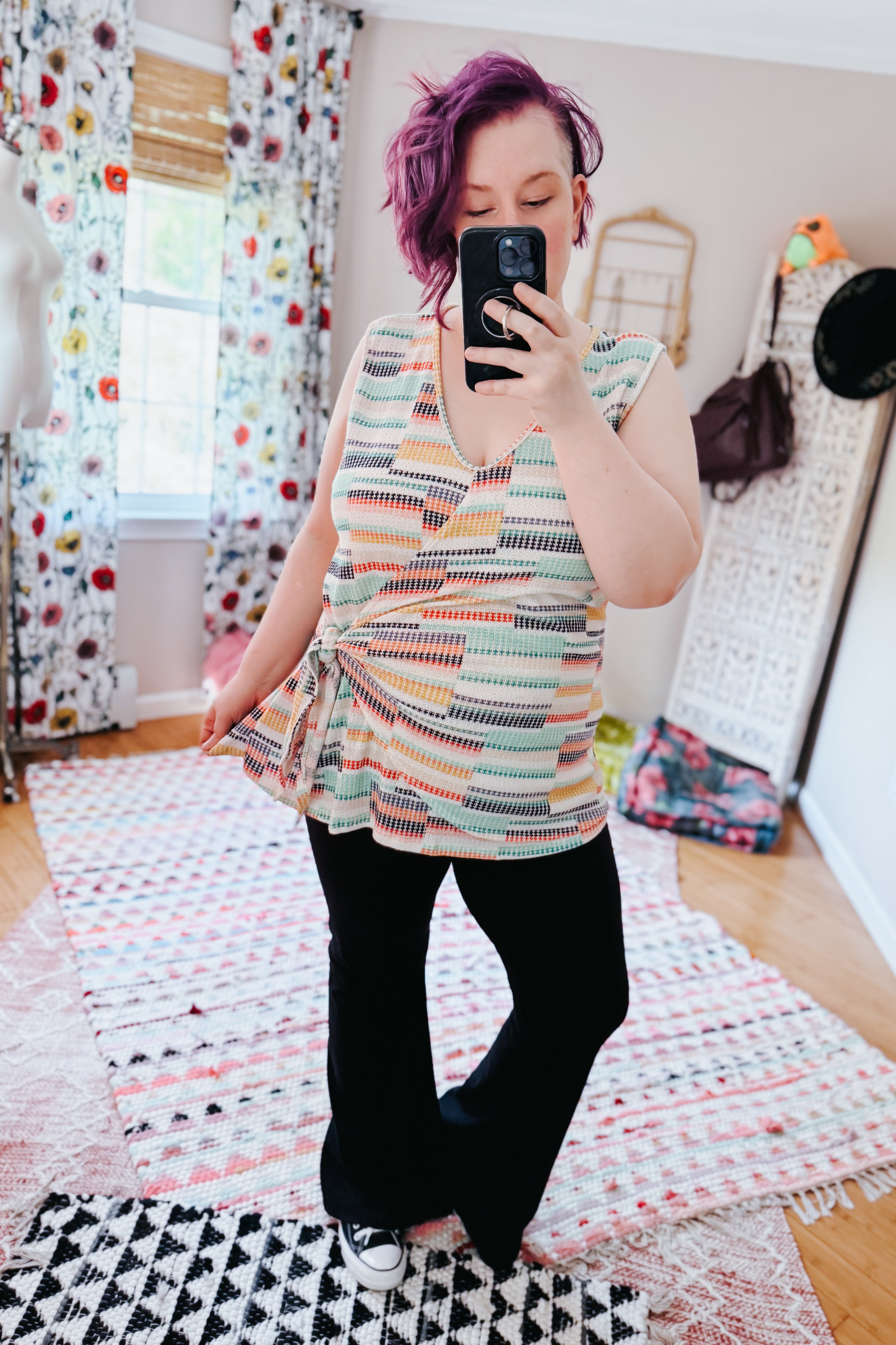 Woman with purple hair wearing a lightweight patterned V-neck tank and black pants in an eclectic, free-spirited room