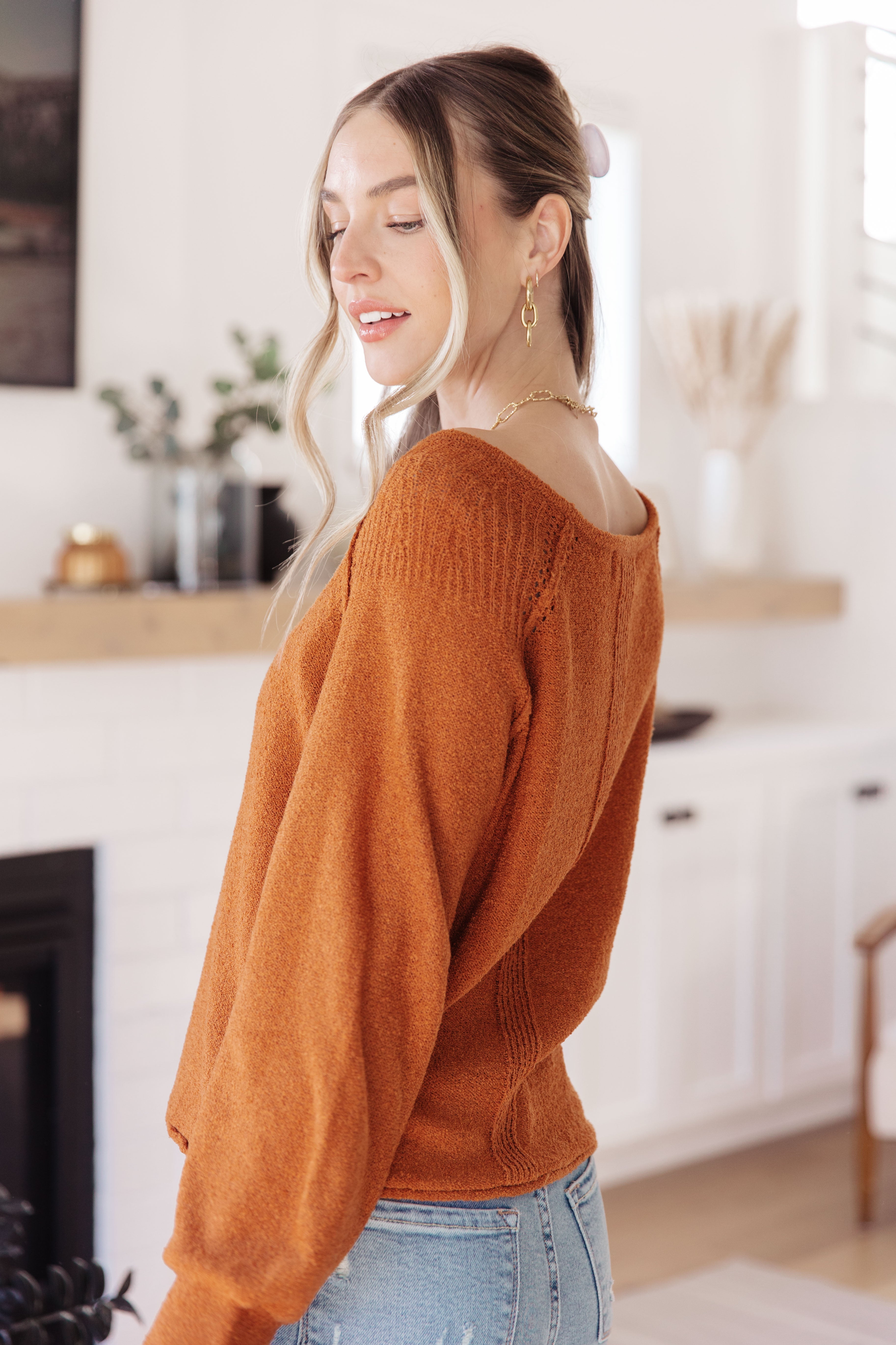Woman with blonde hair wearing textured burnt orange pullover sweater with boat neckline indoors