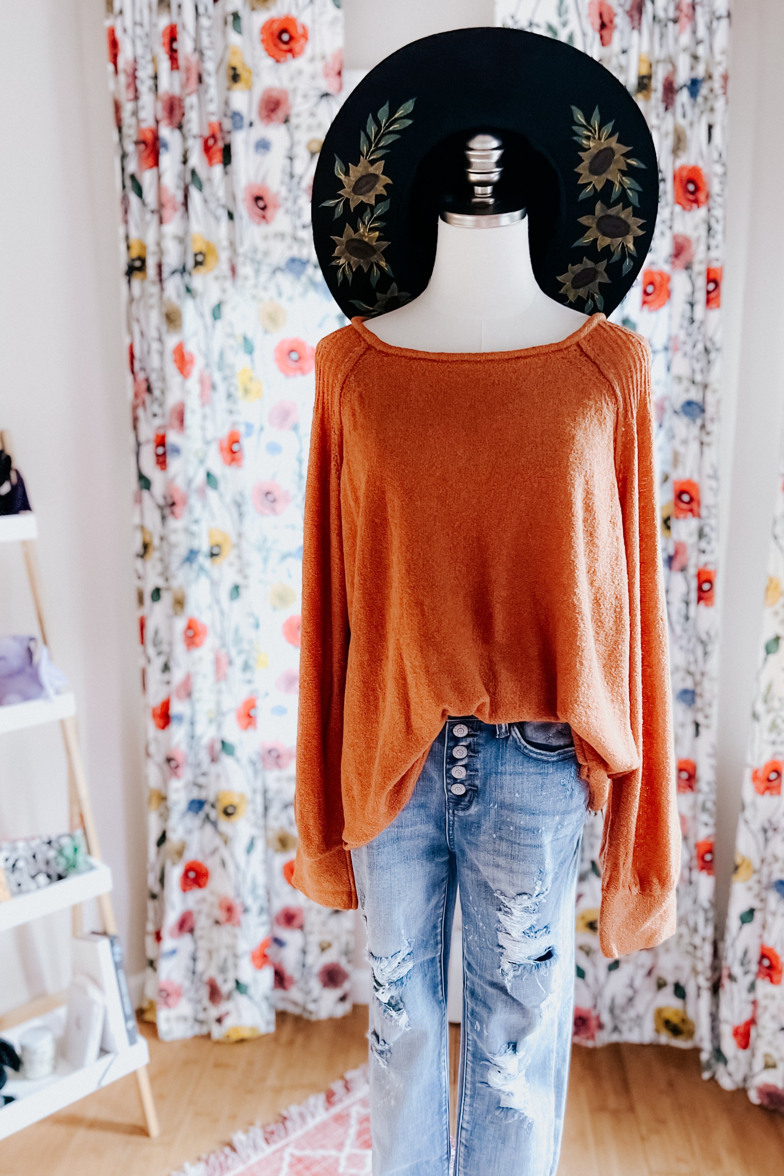 Mannequin wearing orange loose pullover sweater paired with distressed high-rise blue jeans and black sunflower-printed hat