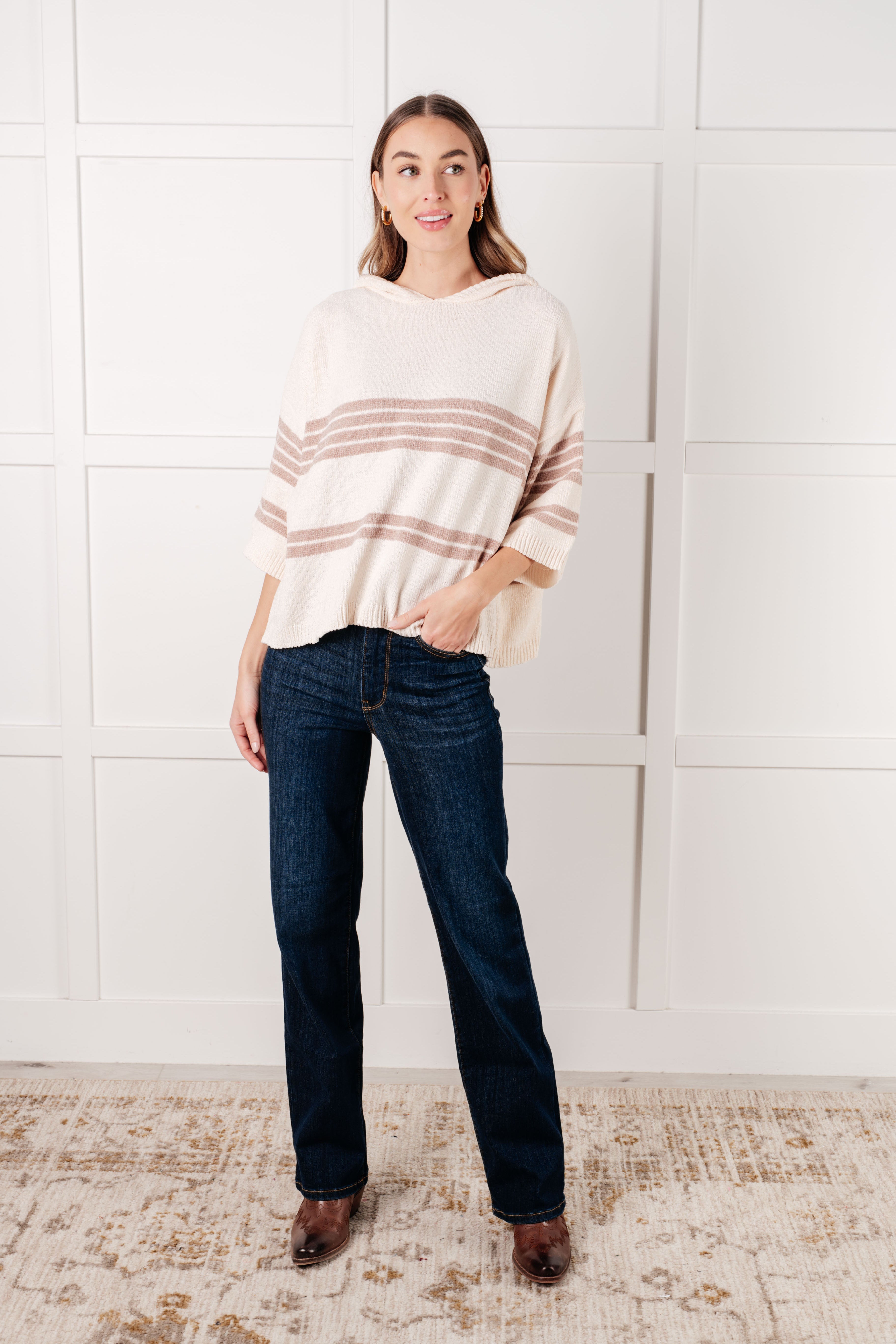 Woman wearing a cream striped hoodie with dark wide-leg jeans indoors