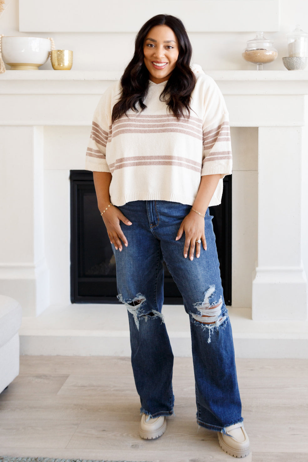 Smiling woman in a cream striped half sleeve hoodie and ripped wide leg jeans indoors