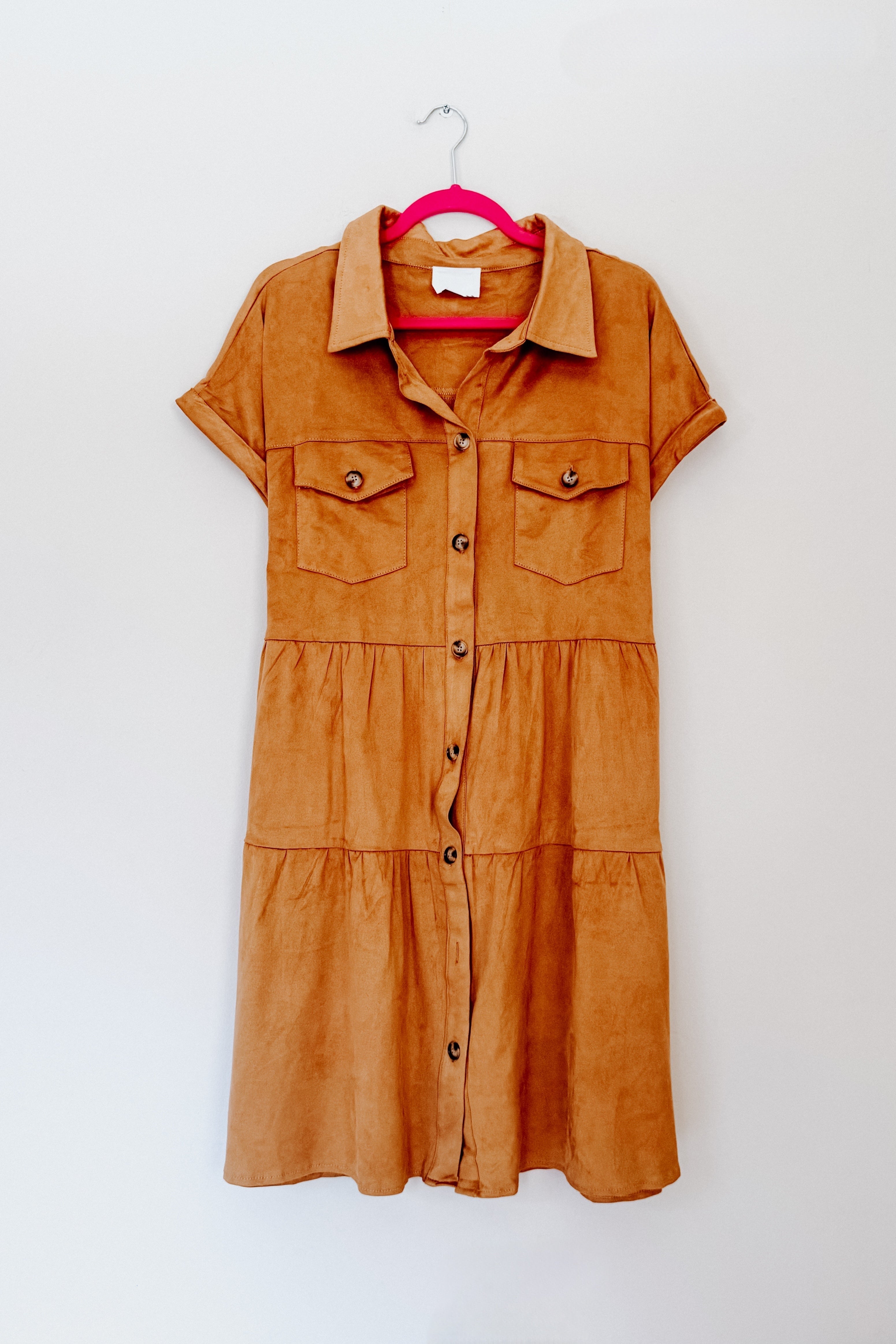 Light brown faux suede short-sleeve shirt dress with button front and two chest pockets hanging on pink hanger