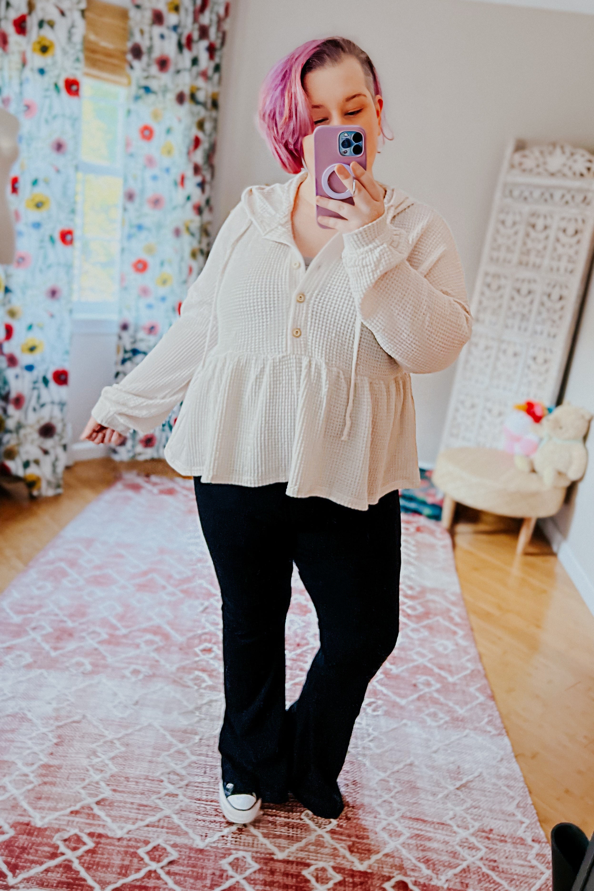 Woman with pink hair taking mirror selfie wearing off-white waffle knit hoodie with buttons and flared hem paired with black pants