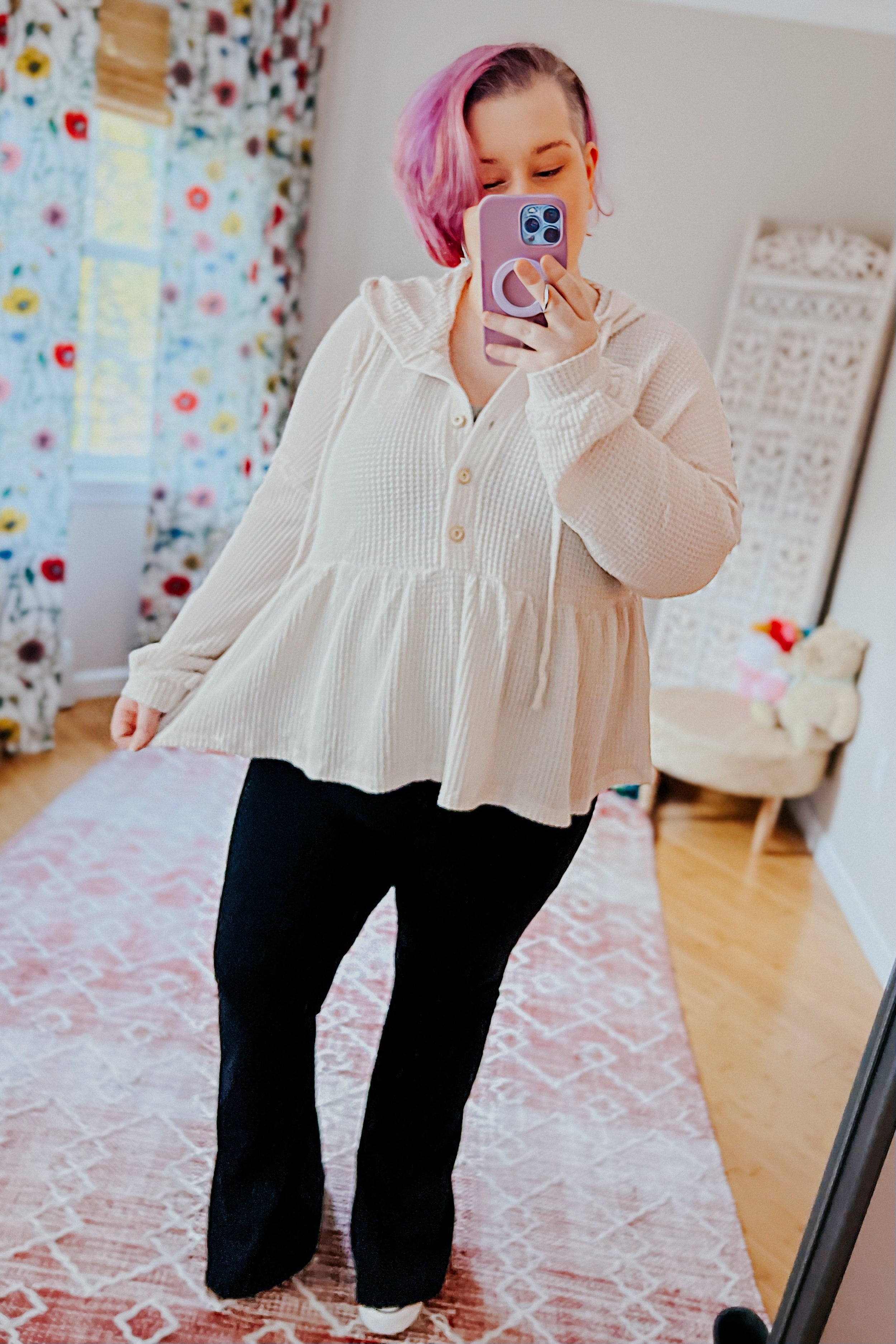 Woman with pink hair wearing off-white waffle knit hoodie with buttons and peplum hem taking mirror selfie indoors