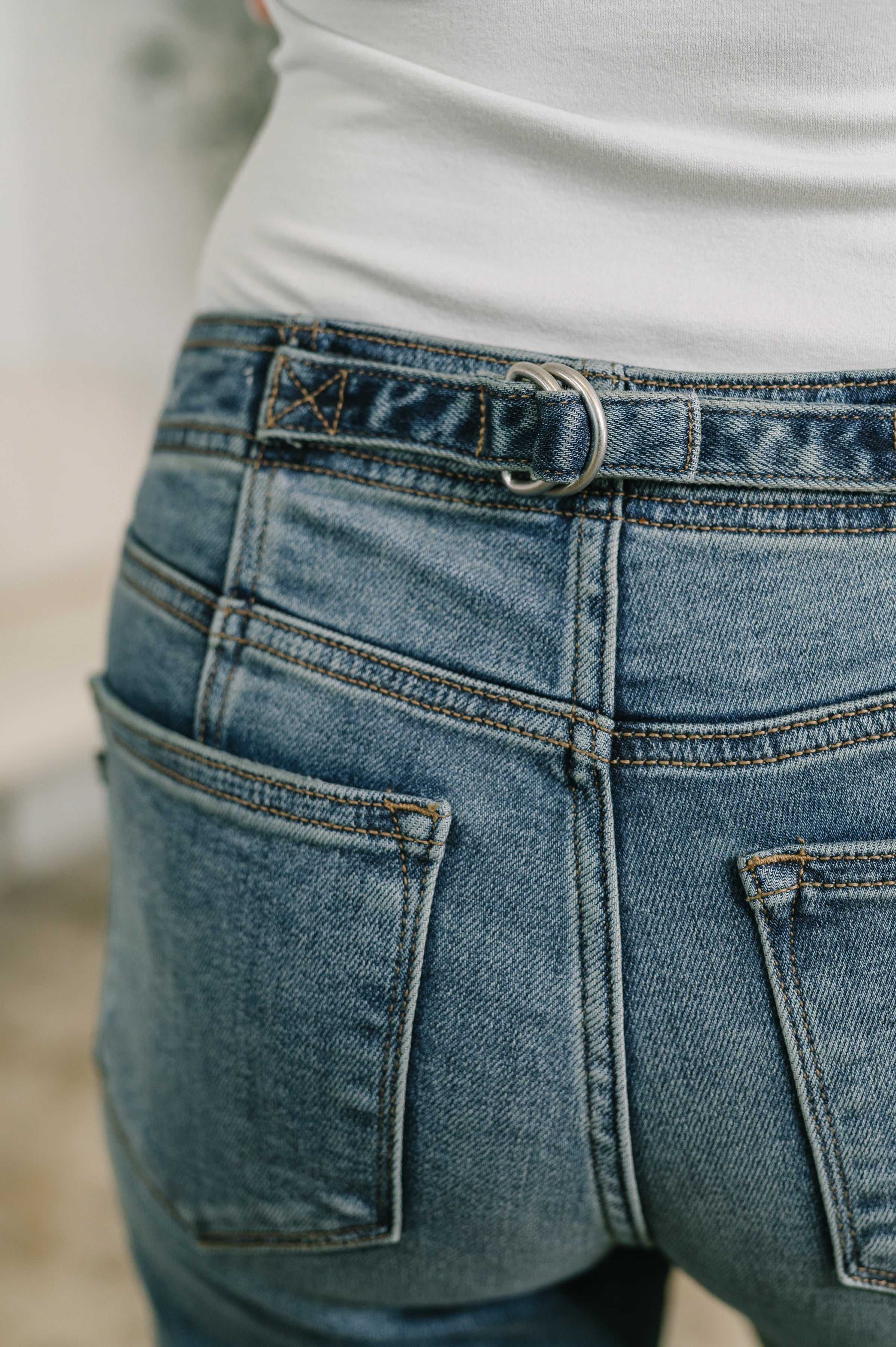 Close-up of blue mid rise boyfriend jeans with belt detail worn with white top in a relaxed setting