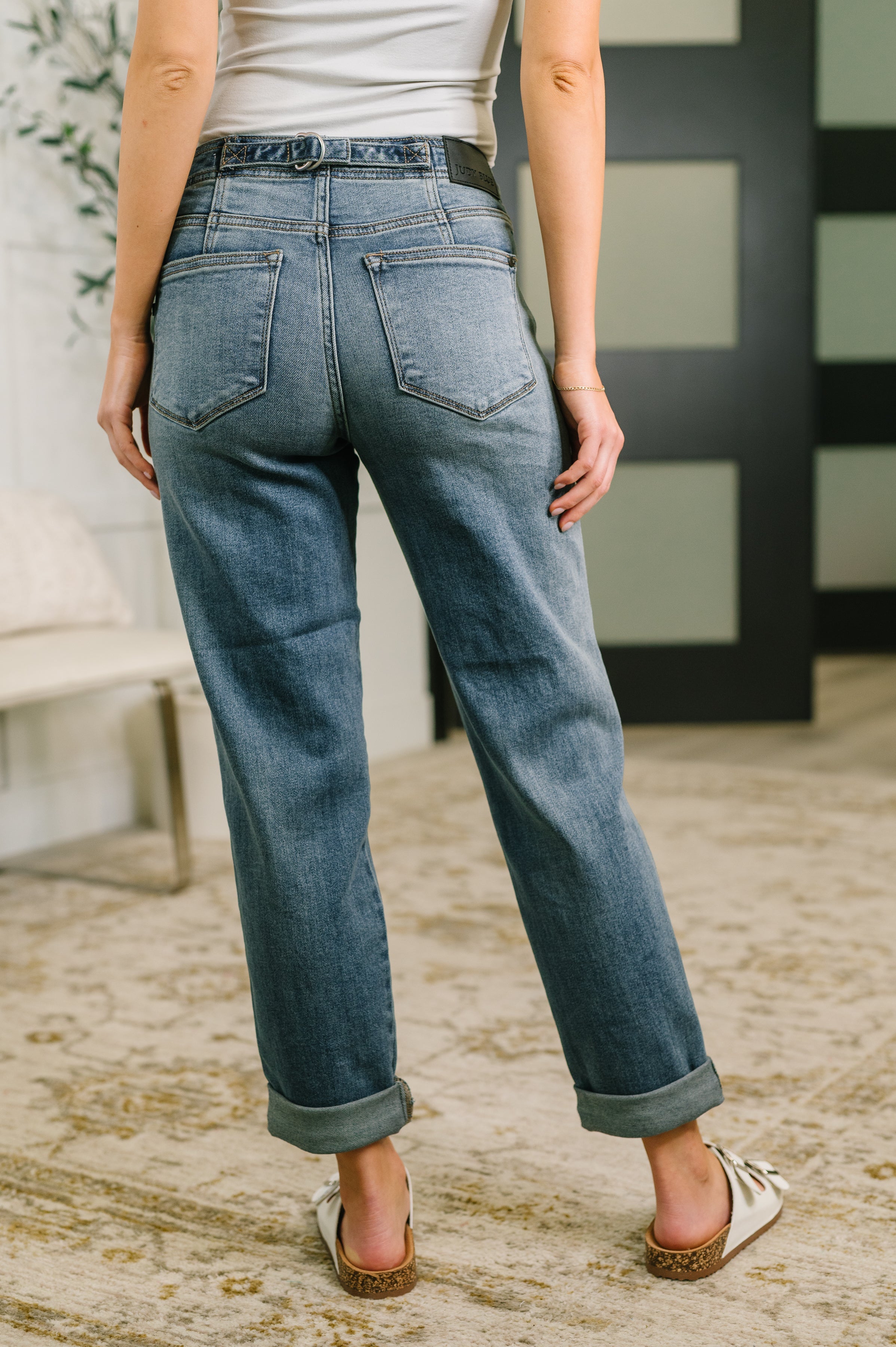Back view of woman wearing blue mid rise boyfriend jeans with rolled cuffs and a white tank top indoors