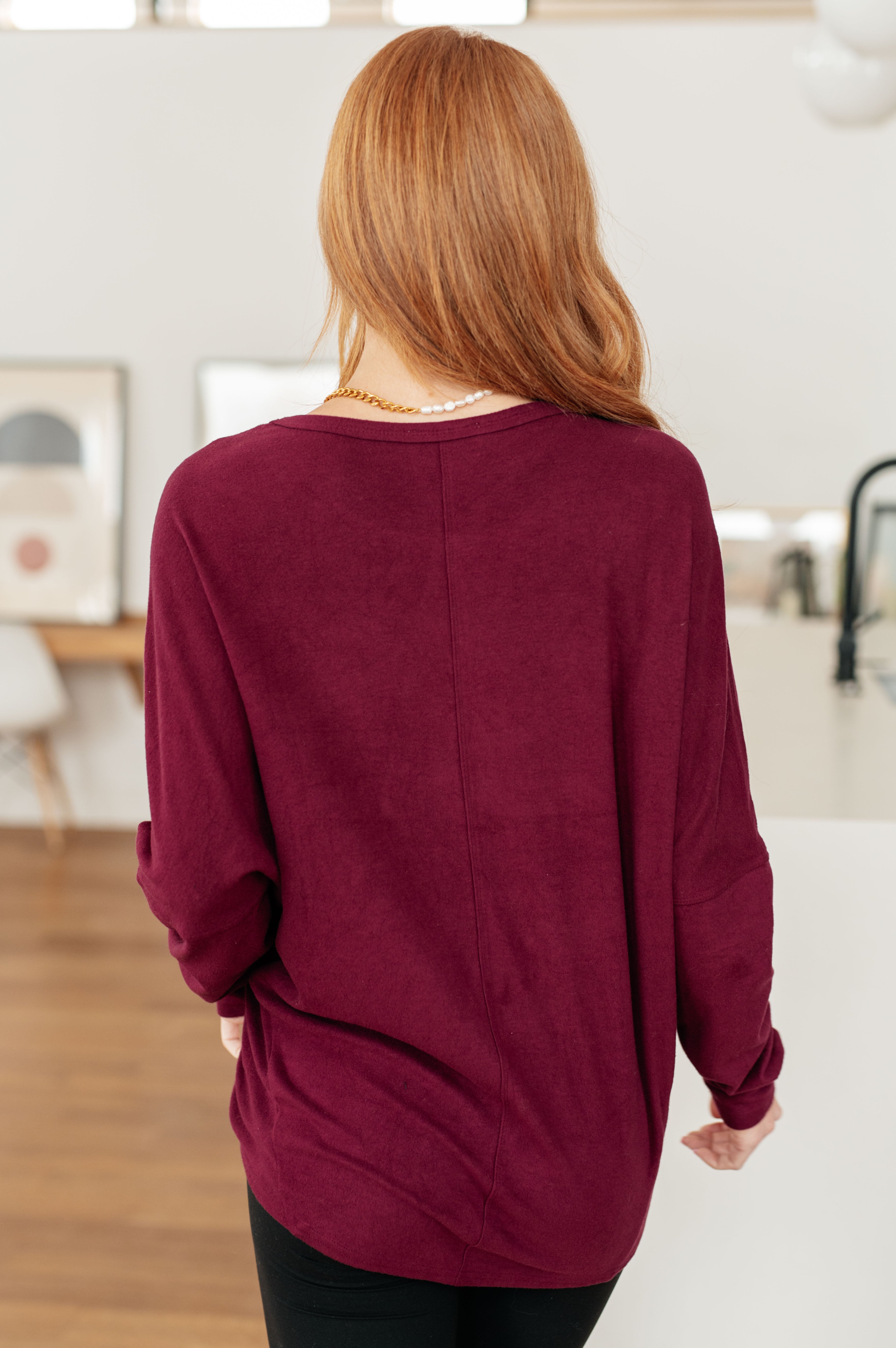 Back view of woman with red hair wearing loose wine-colored dolman sleeve top indoors