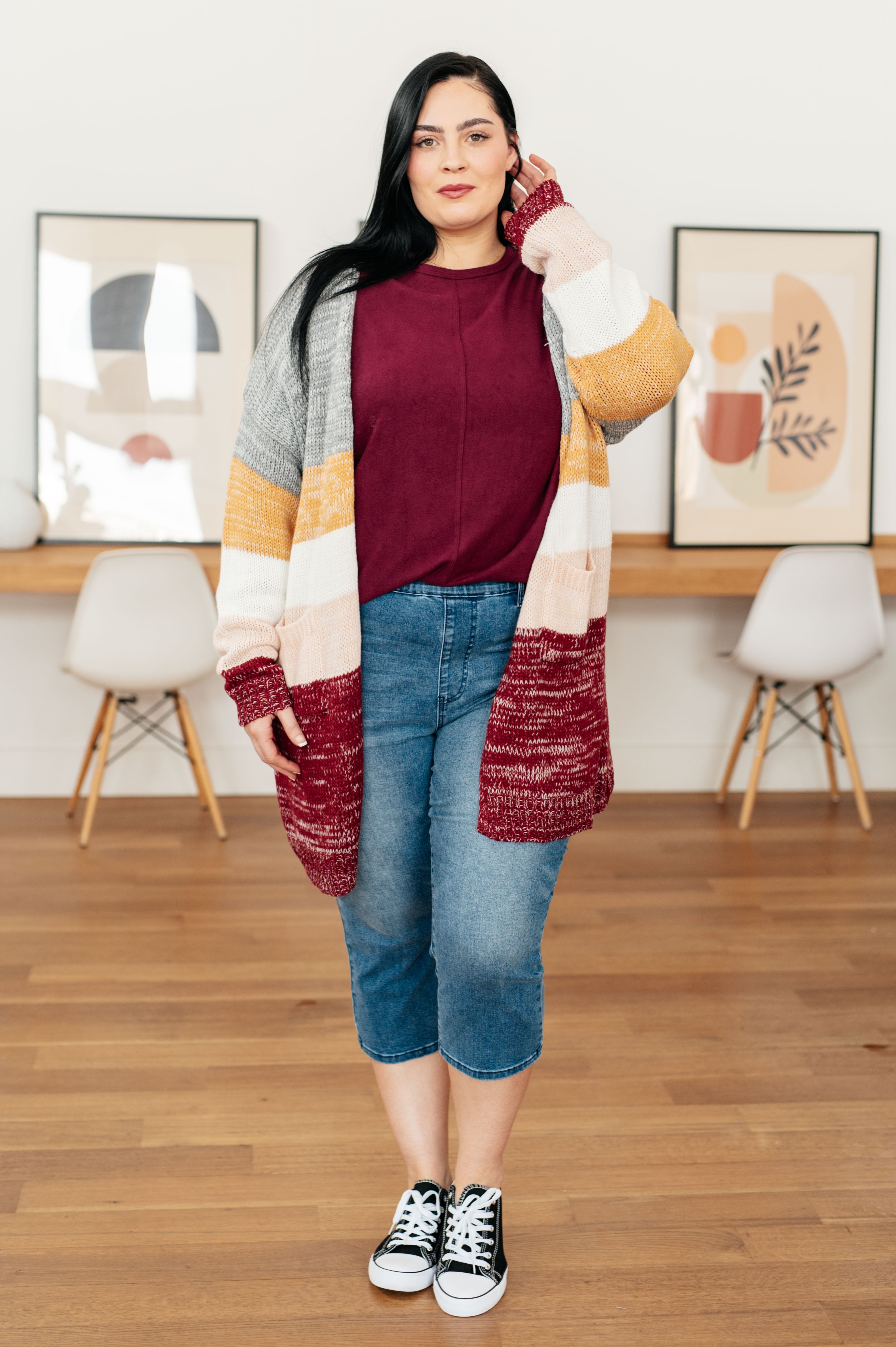 Woman with long black hair wearing wine-colored dolman sleeve top and striped multi-color cardigan indoors