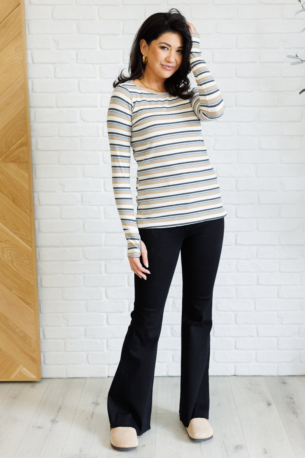 Woman wearing a blue, beige, and white striped long-sleeve top with thumbholes paired with black flare pants indoors