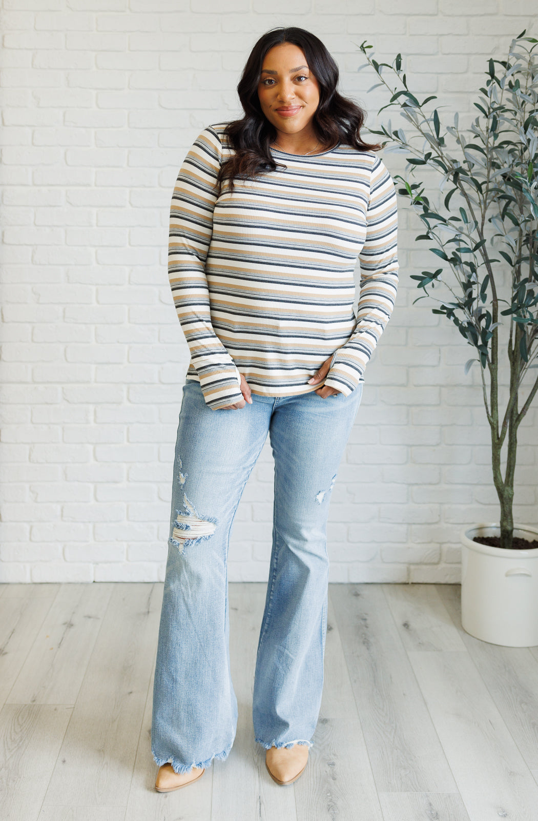 Woman wearing a blue striped ribbed long-sleeve top with thumbholes paired with light distressed flare jeans indoors