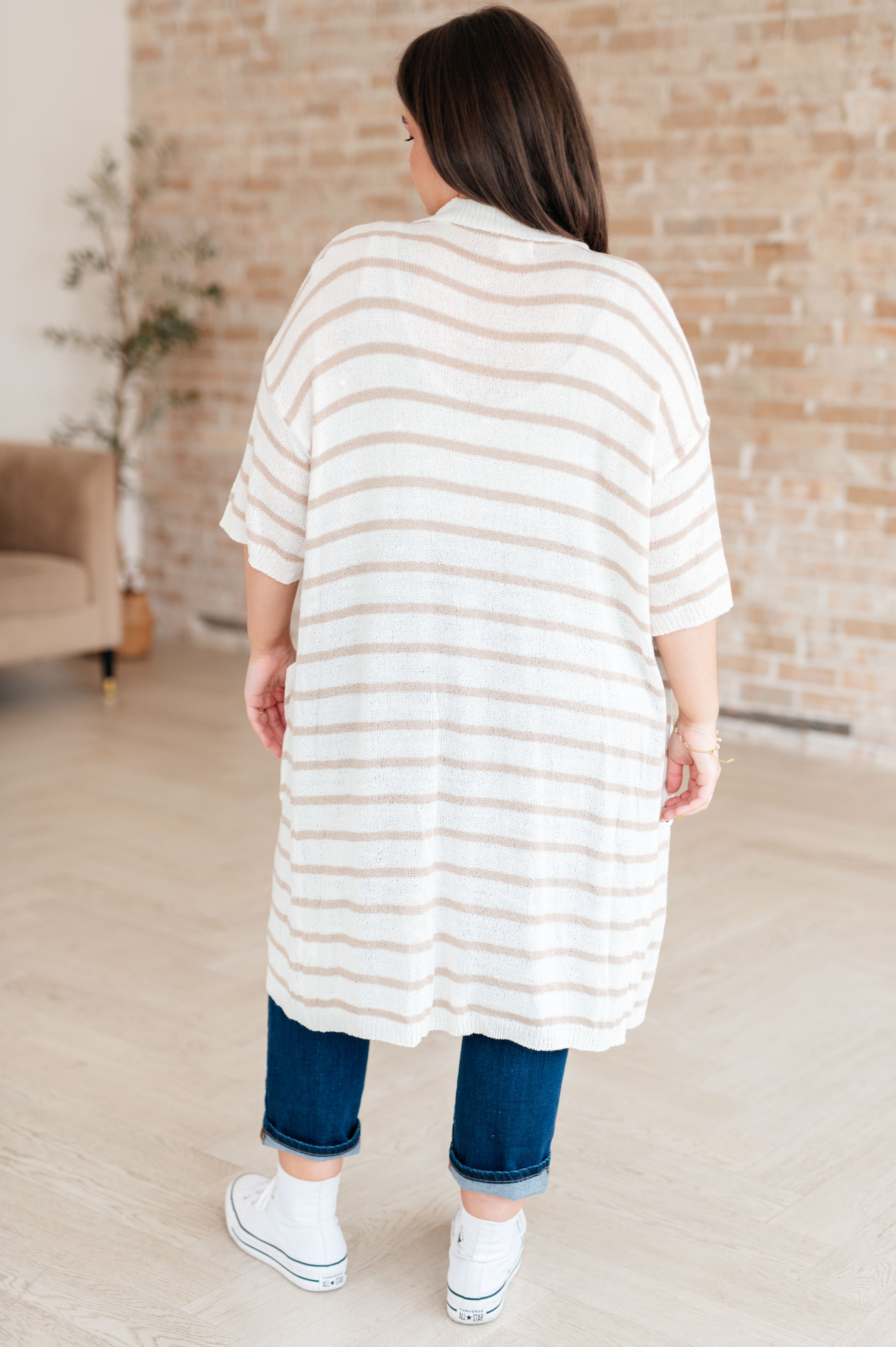 Woman modeling white and beige striped button-up collared dress from the back with rolled jeans and white sneakers