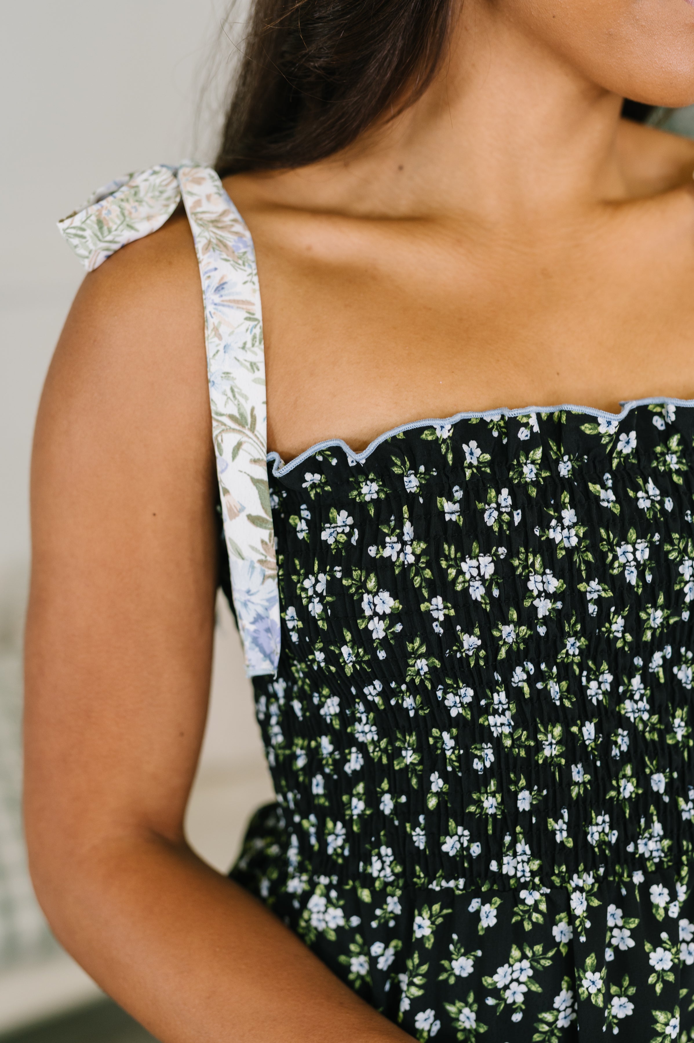 Close-up of navy tiered maxi dress with smocked bodice and contrast floral tie shoulder strap on model