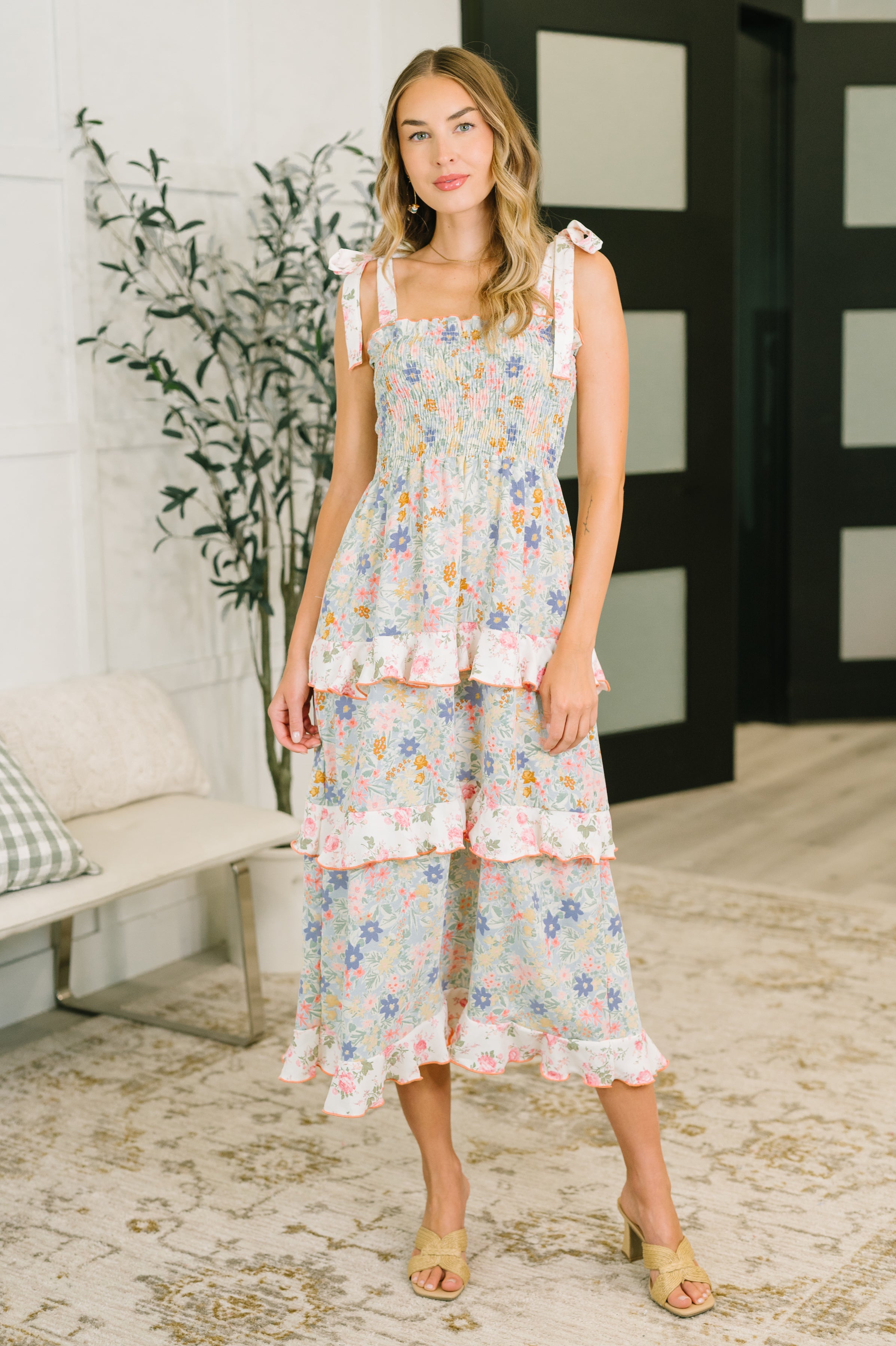 Woman wearing sleeveless floral midi dress with tiered ruffles and tied shoulder straps indoors