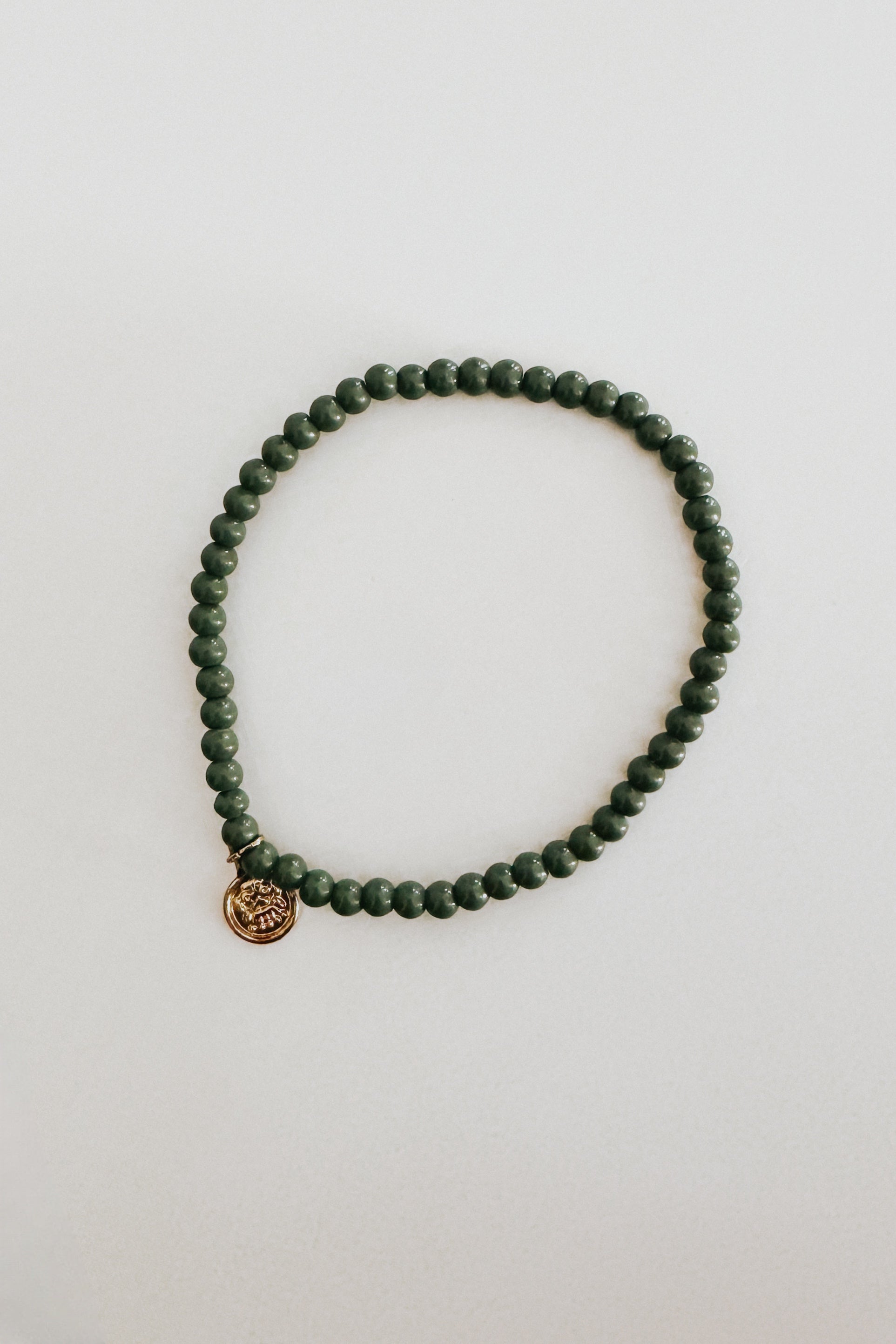 Single strand green beaded bracelet with small gold charm laid flat on a neutral light background